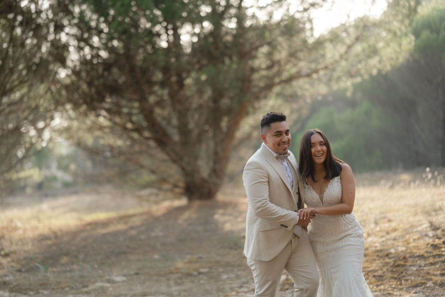 Newlyweds share a romantic moment while walking together on a sunlit forest trail.