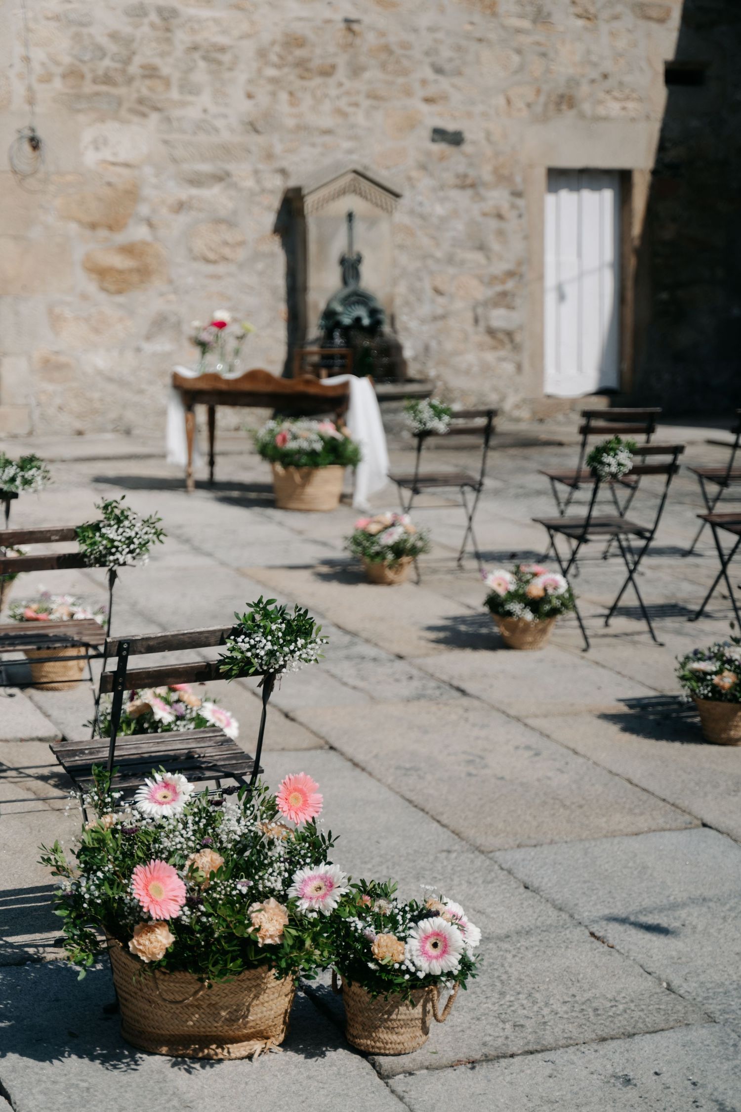 Stone courtyard with bistro chairs and pink floral arrangements in woven baskets.