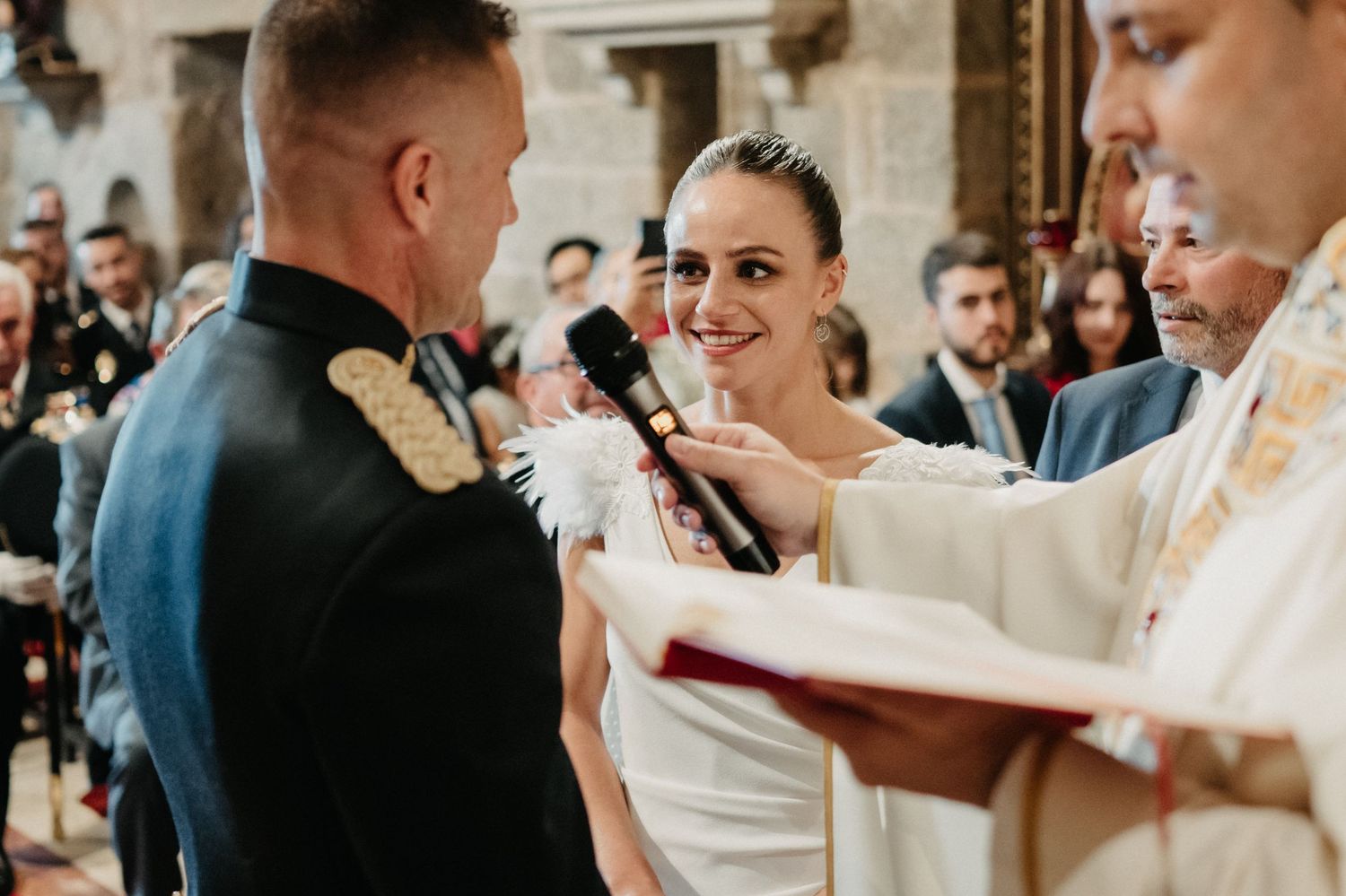 Military wedding ceremony with bride in white dress and uniformed groom exchanging vows at altar.