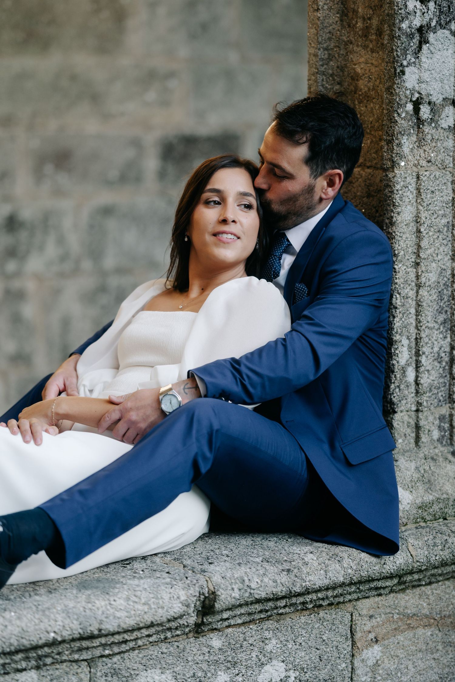 A couple in wedding attire shares an intimate moment while reclining on stone steps in an artistic photo series.
