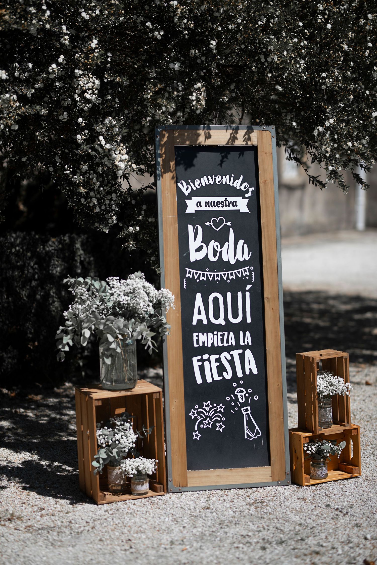 Rustic wooden crates and chalkboard signs with Spanish text create a charming wedding decor display in an outdoor setting.