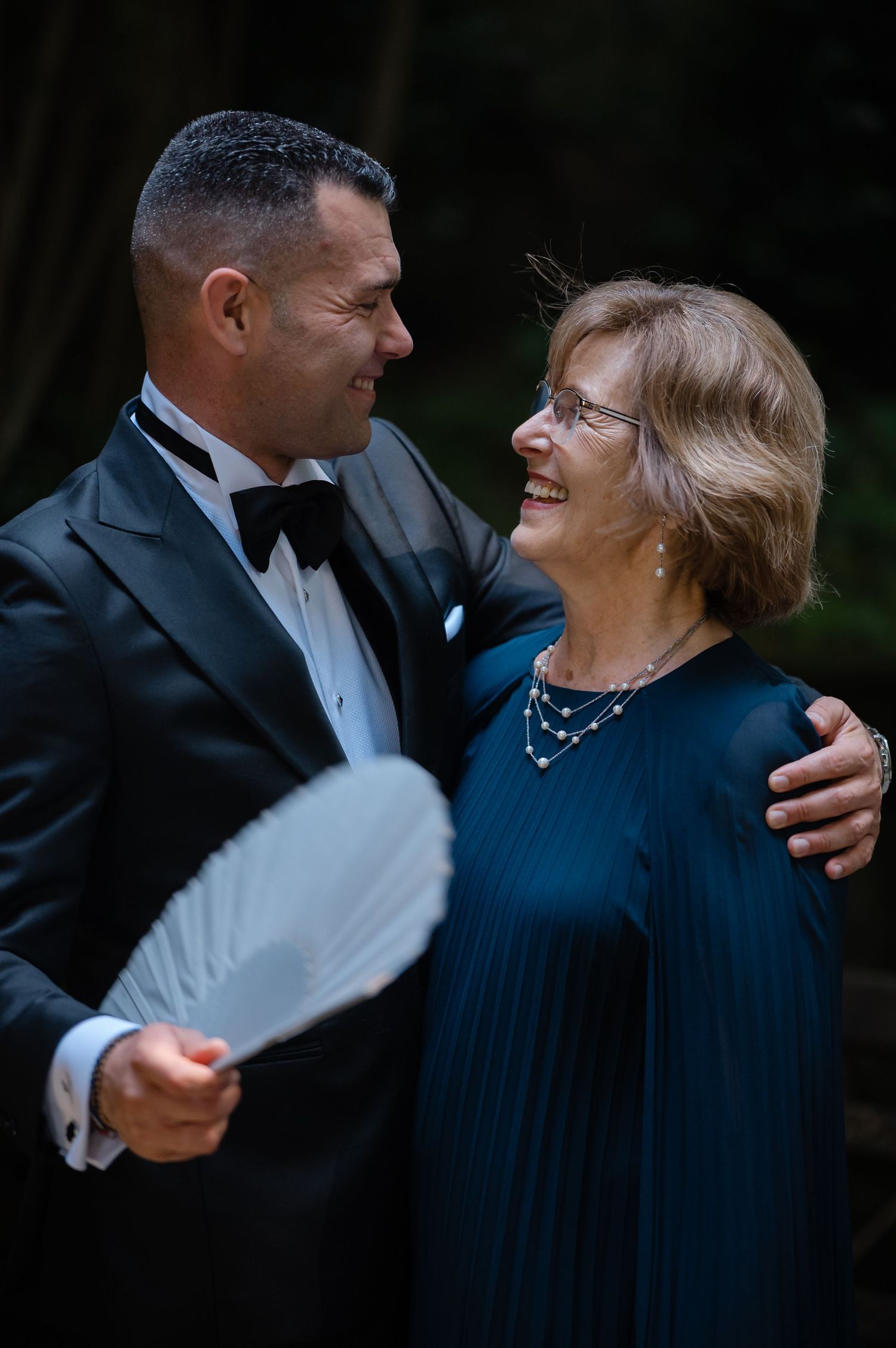 A couple in formal attire share a tender dance moment together in a dark setting.