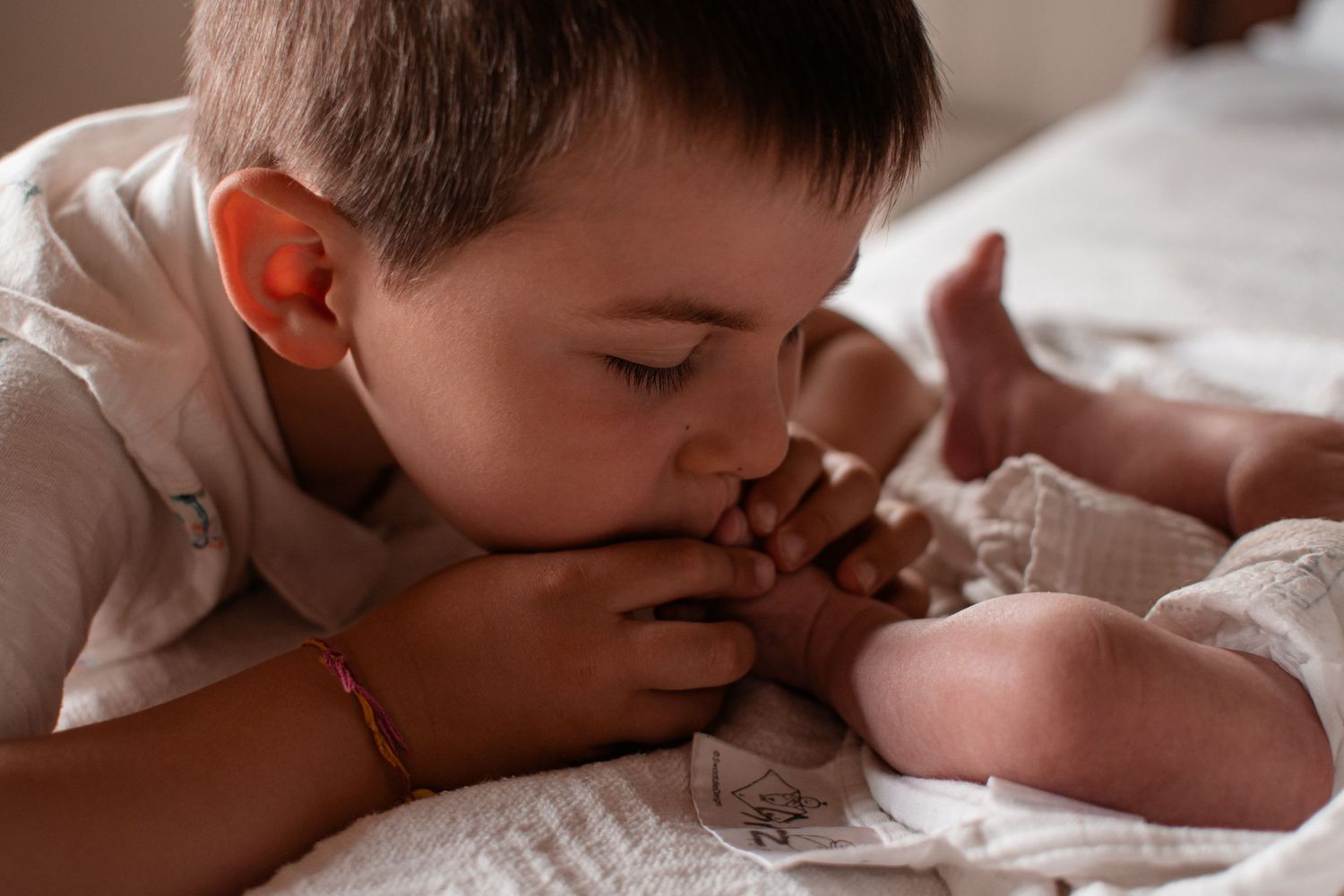 Sweet sibling portrait of young boy kissing newborn baby in warm natural light.