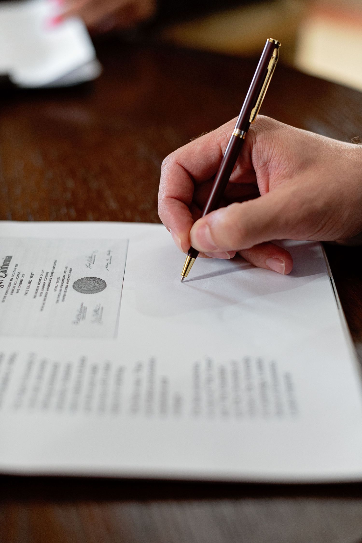 Close-up of a hand signing an official legal document with a gold-tipped pen on a wooden desk.