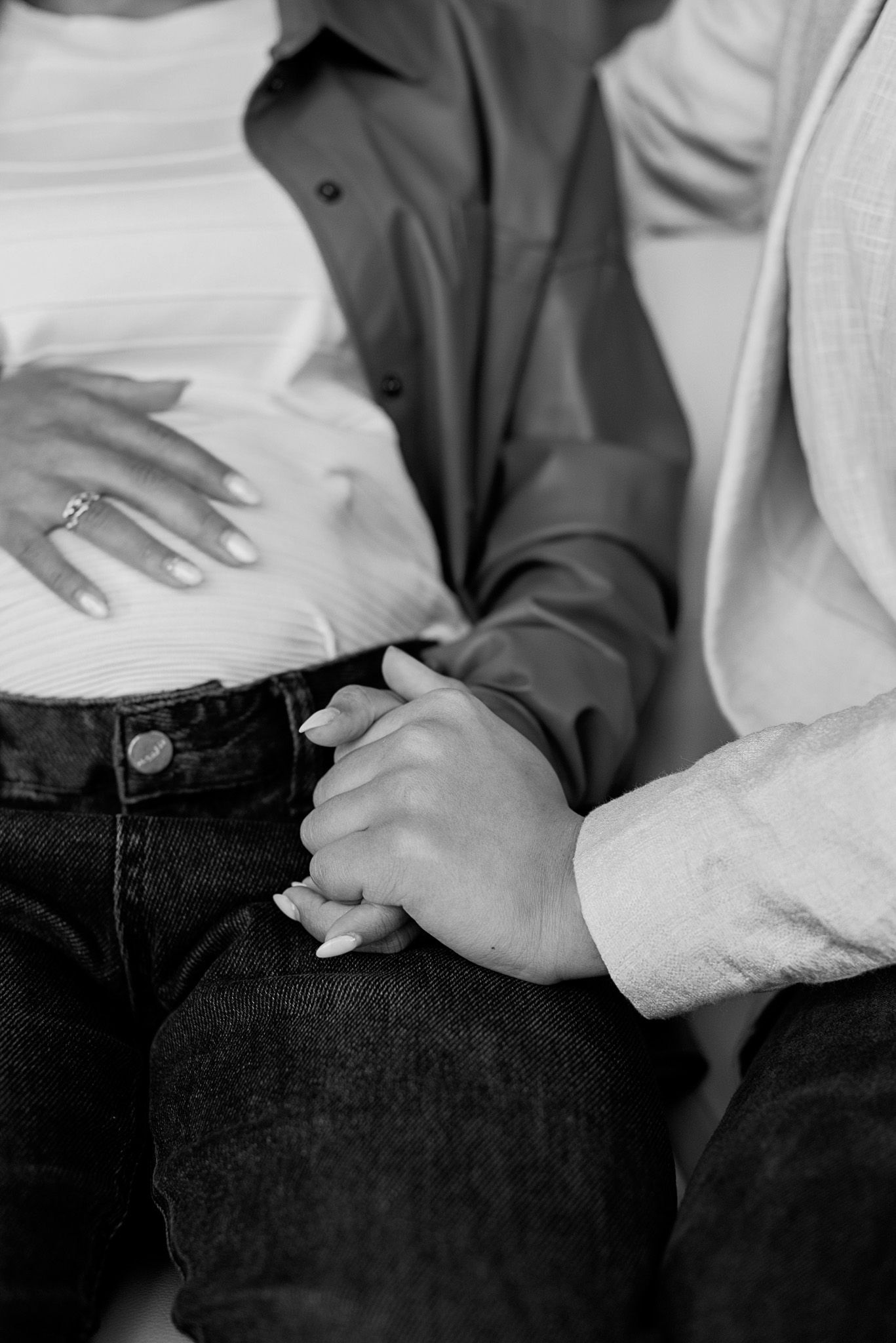 Black and white close-up of a pregnant woman holding her baby bump while her partner holds her hand.