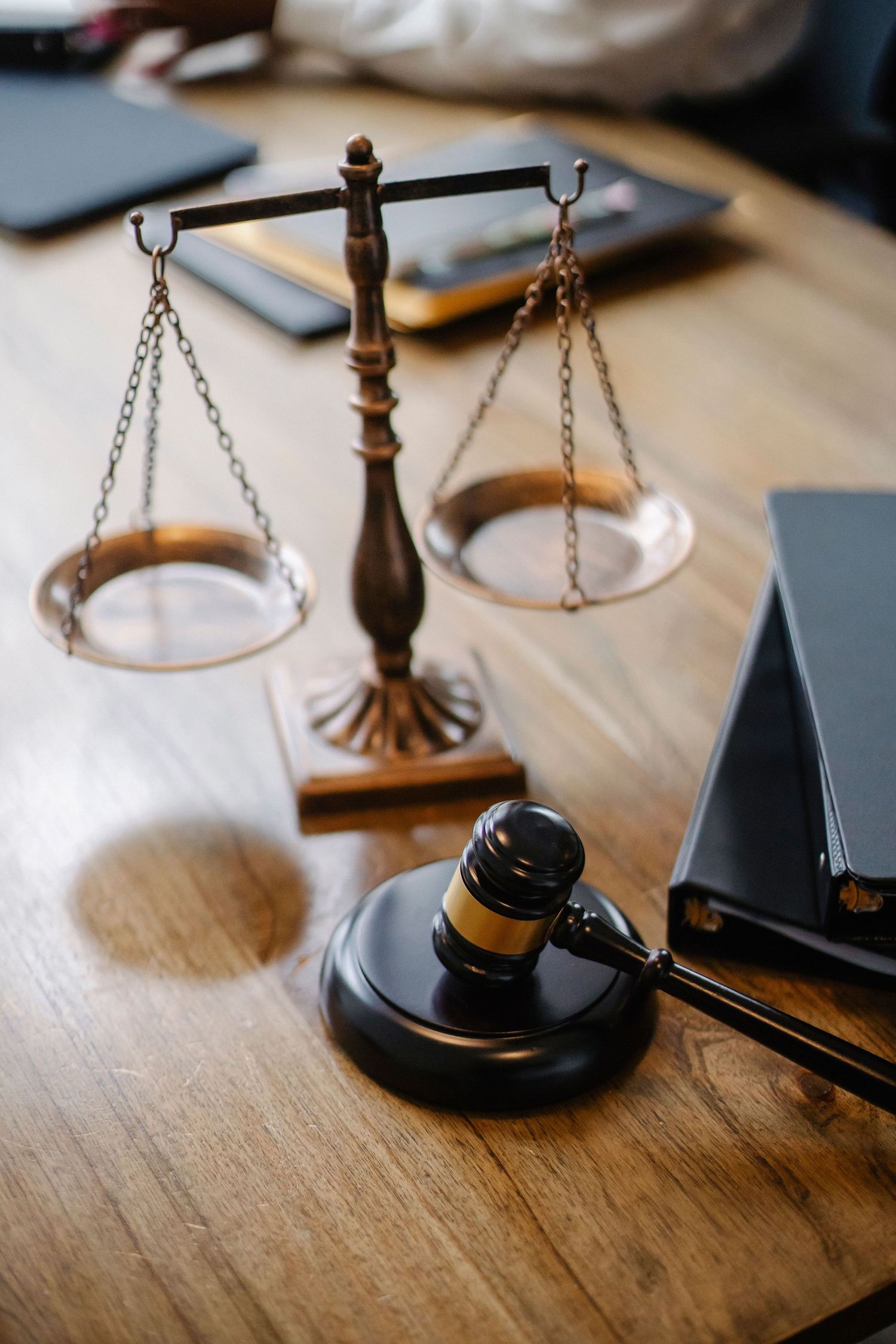 Brass scales of justice and wooden gavel on a wooden desk in a law office setting.