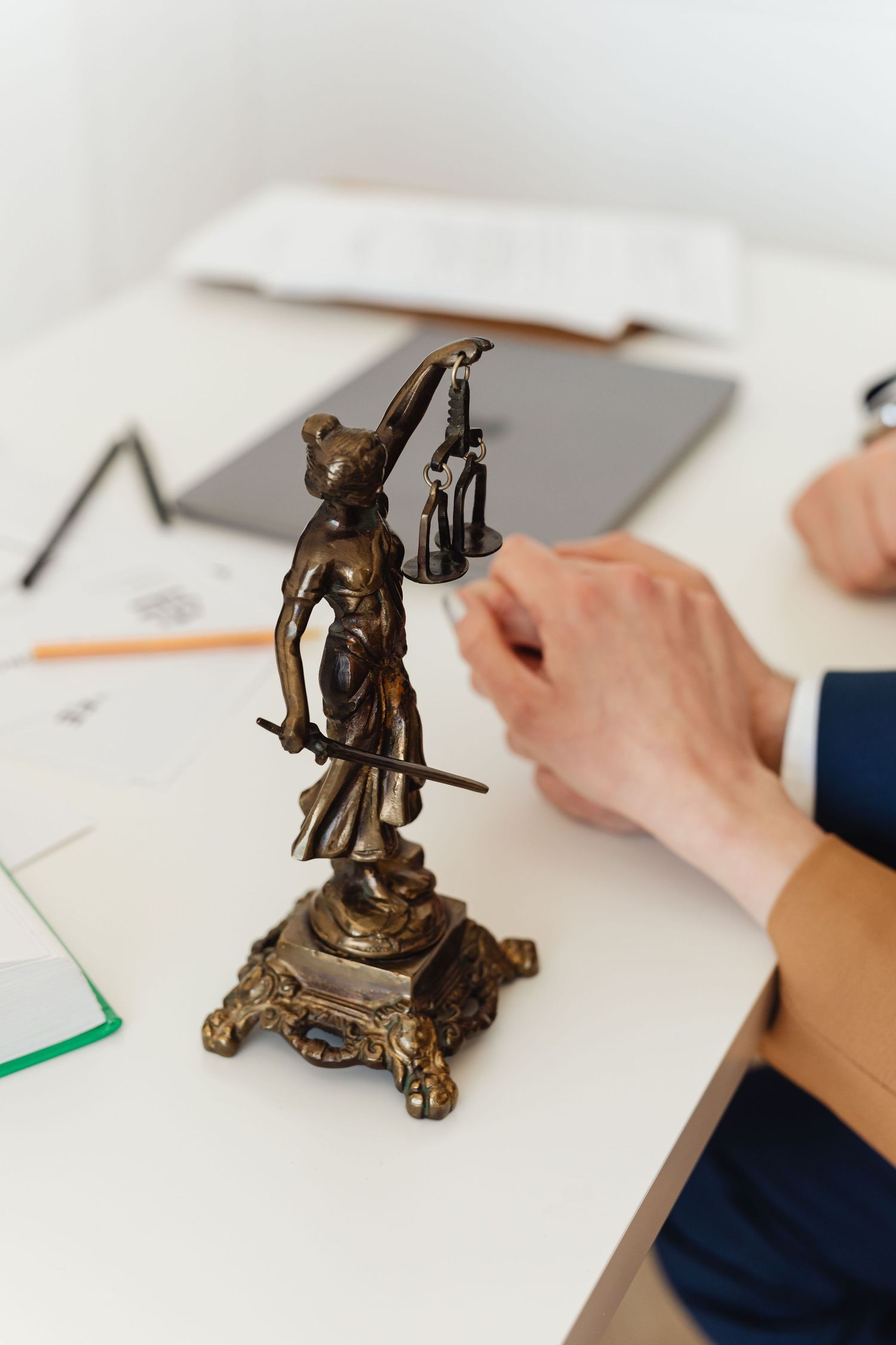 Bronze Lady Justice Themis statue on white desk beside lawyer's hands reviewing legal documents.