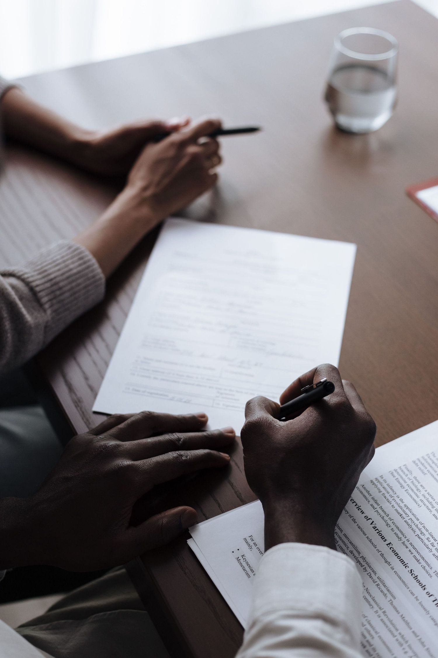 Close-up of two people reviewing and signing a legal document at a wooden desk.
