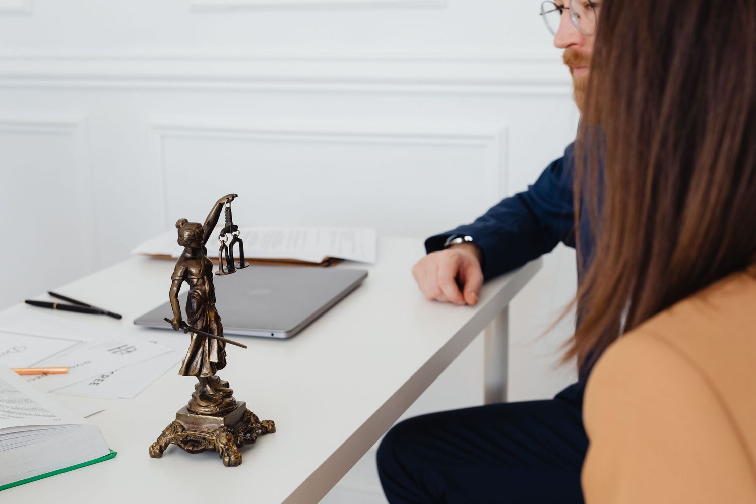 Lady Justice bronze statue on desk during legal consultation between lawyer and client.