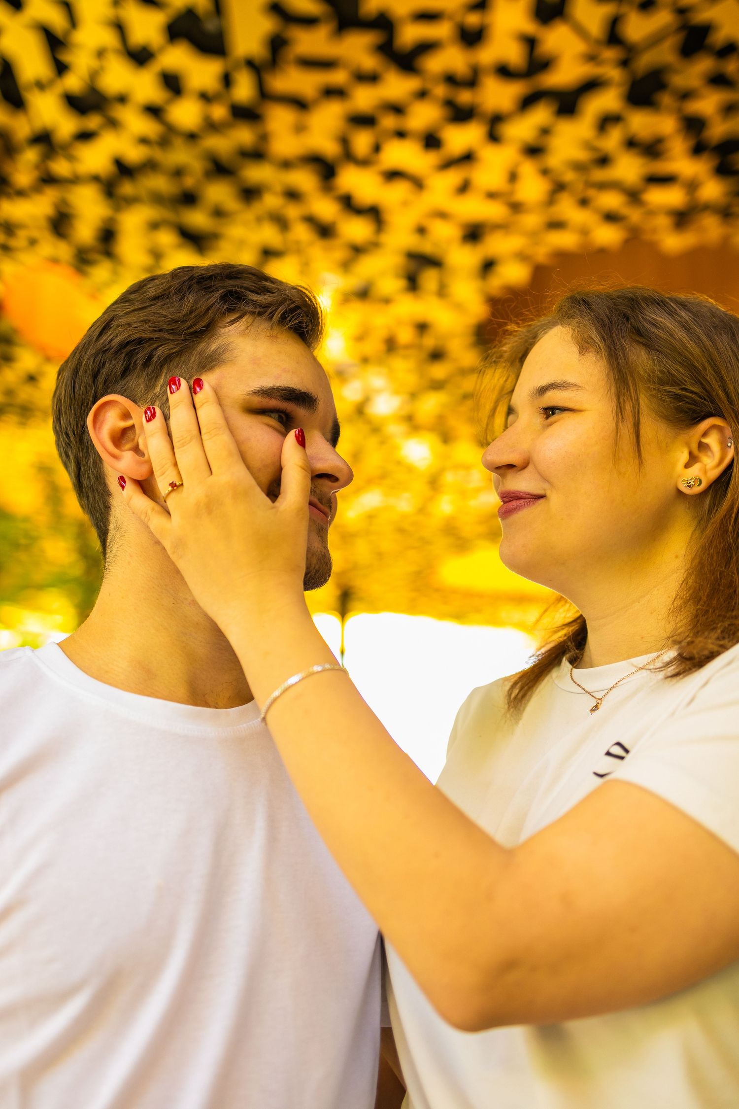 Young couple in white t-shirts sharing a tender moment, woman gently covering man's face with her hand.