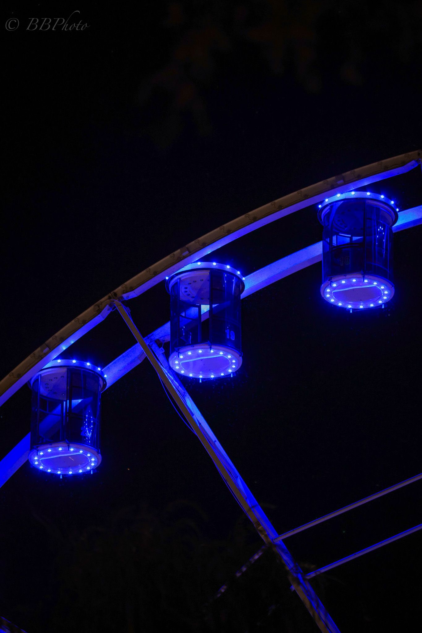 Ferris wheel gondolas illuminated with blue LED lights against a dark night sky at an amusement park.