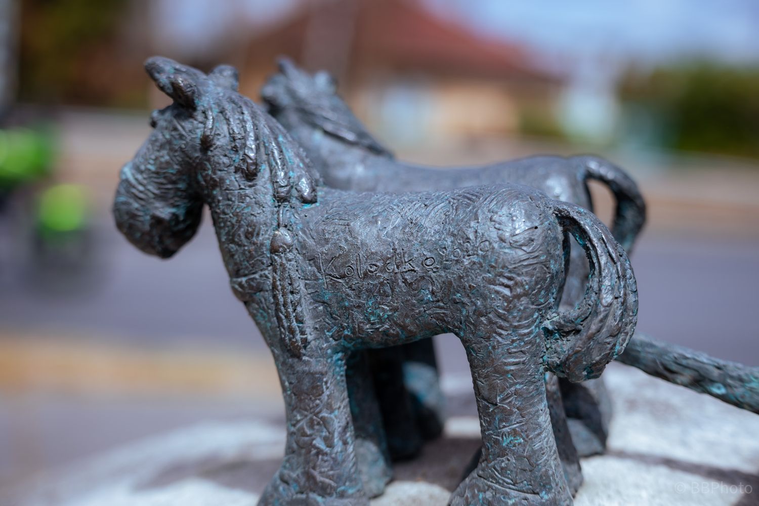 Close-up of a detailed bronze horse sculpture with patina finish, with a blurred street background.