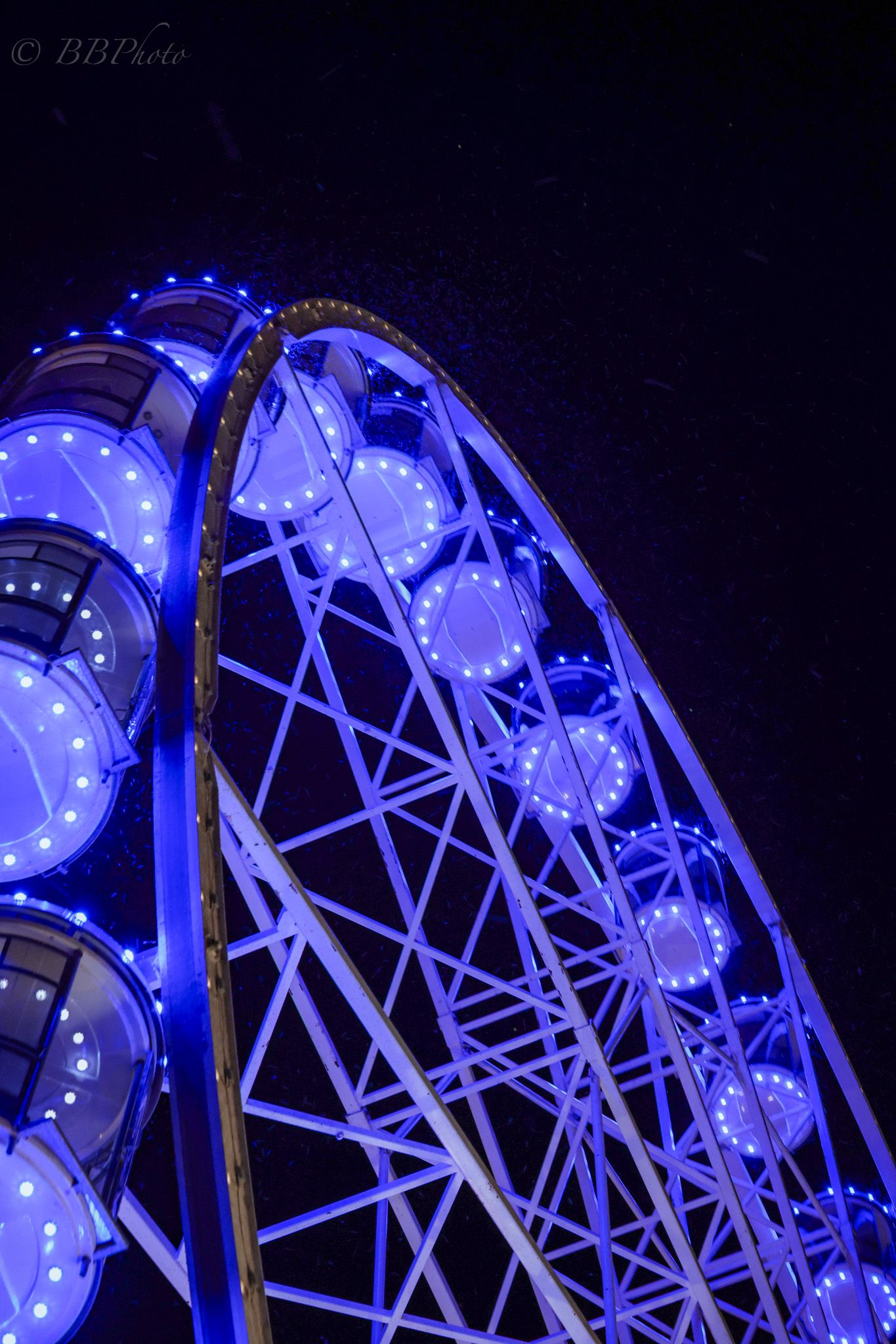 Blue illuminated Ferris wheel glowing against dark night sky, shot from below at dramatic upward angle.