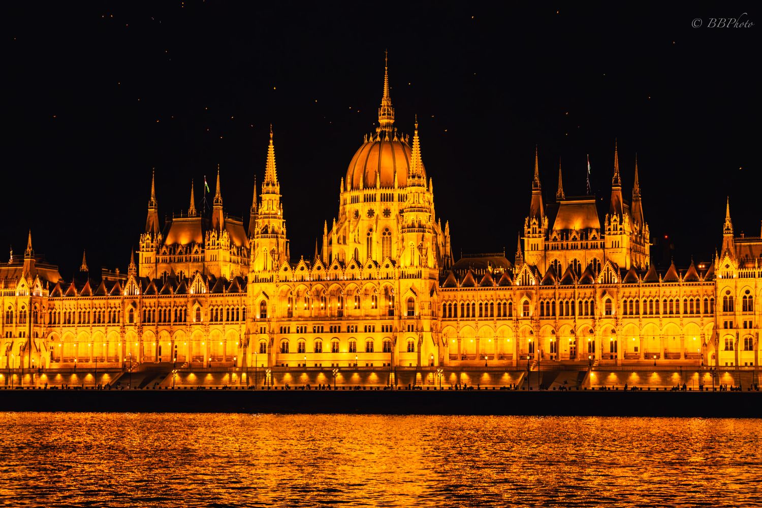 Golden illuminated Hungarian Parliament Building reflecting on the Danube River at night in Budapest.