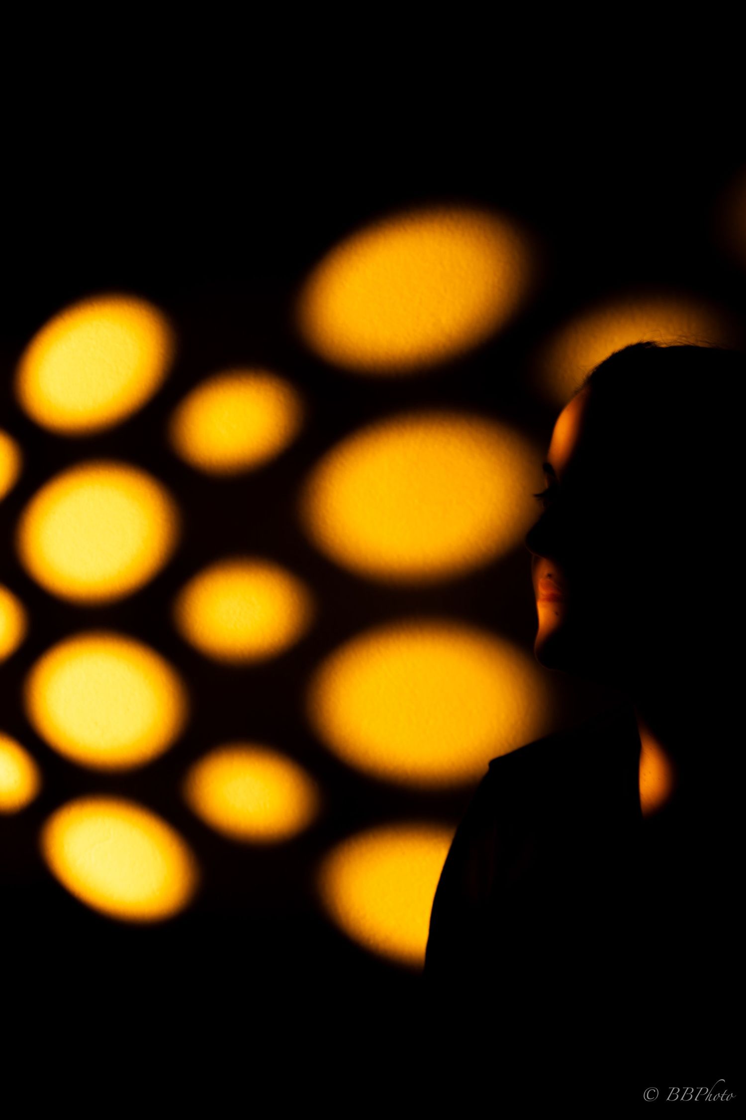 Silhouette of a person against a dark background with glowing golden orange oval light patterns.