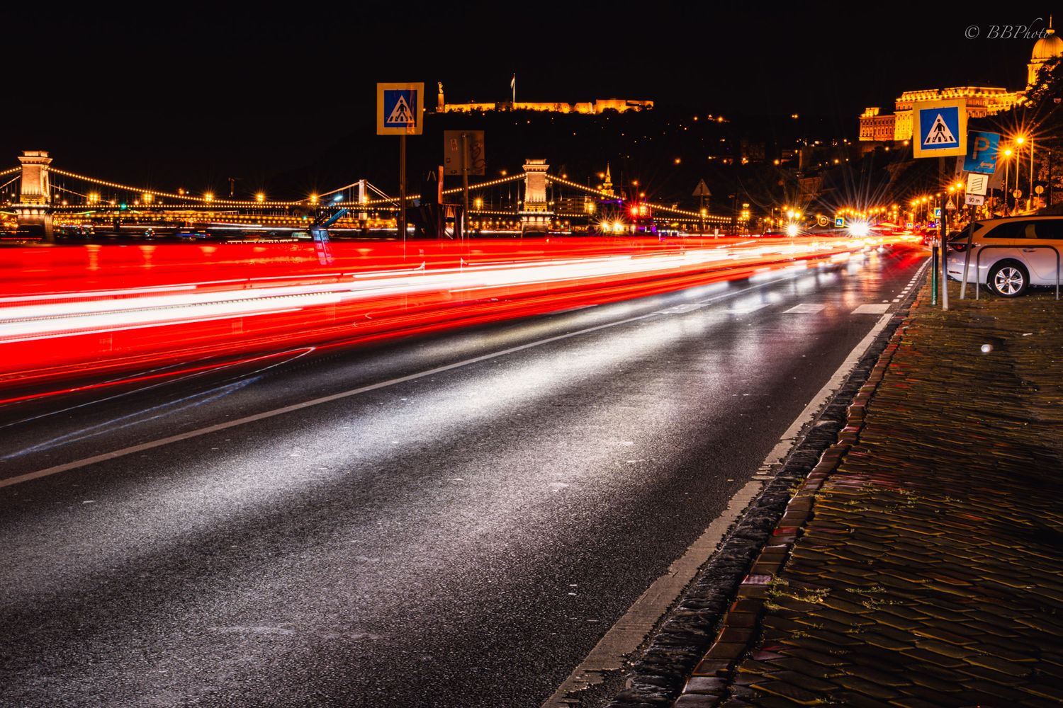 Night long-exposure photo of Budapest road with red and white light trails near Chain Bridge.