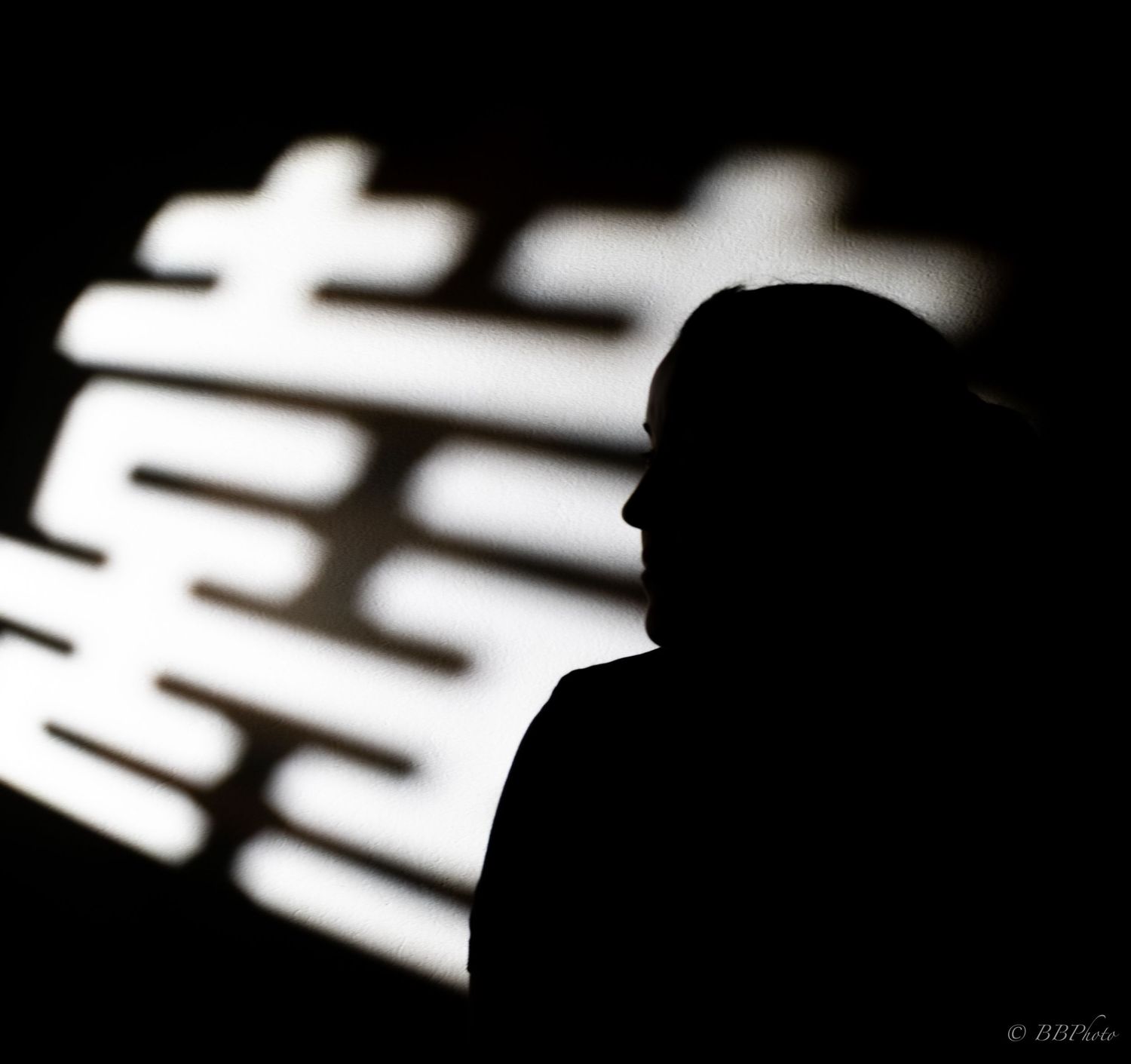 Silhouette of a person against a glowing white Chinese double happiness symbol on a dark background.