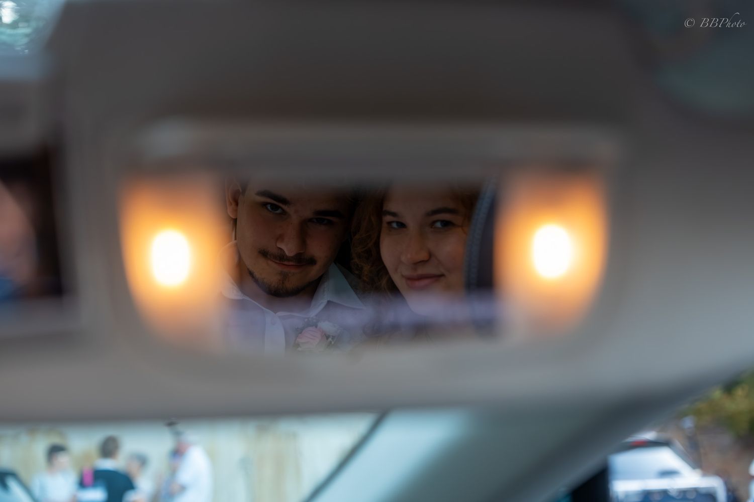 Couple smiling together reflected in a car visor mirror with warm lights, captured in a romantic candid photo.