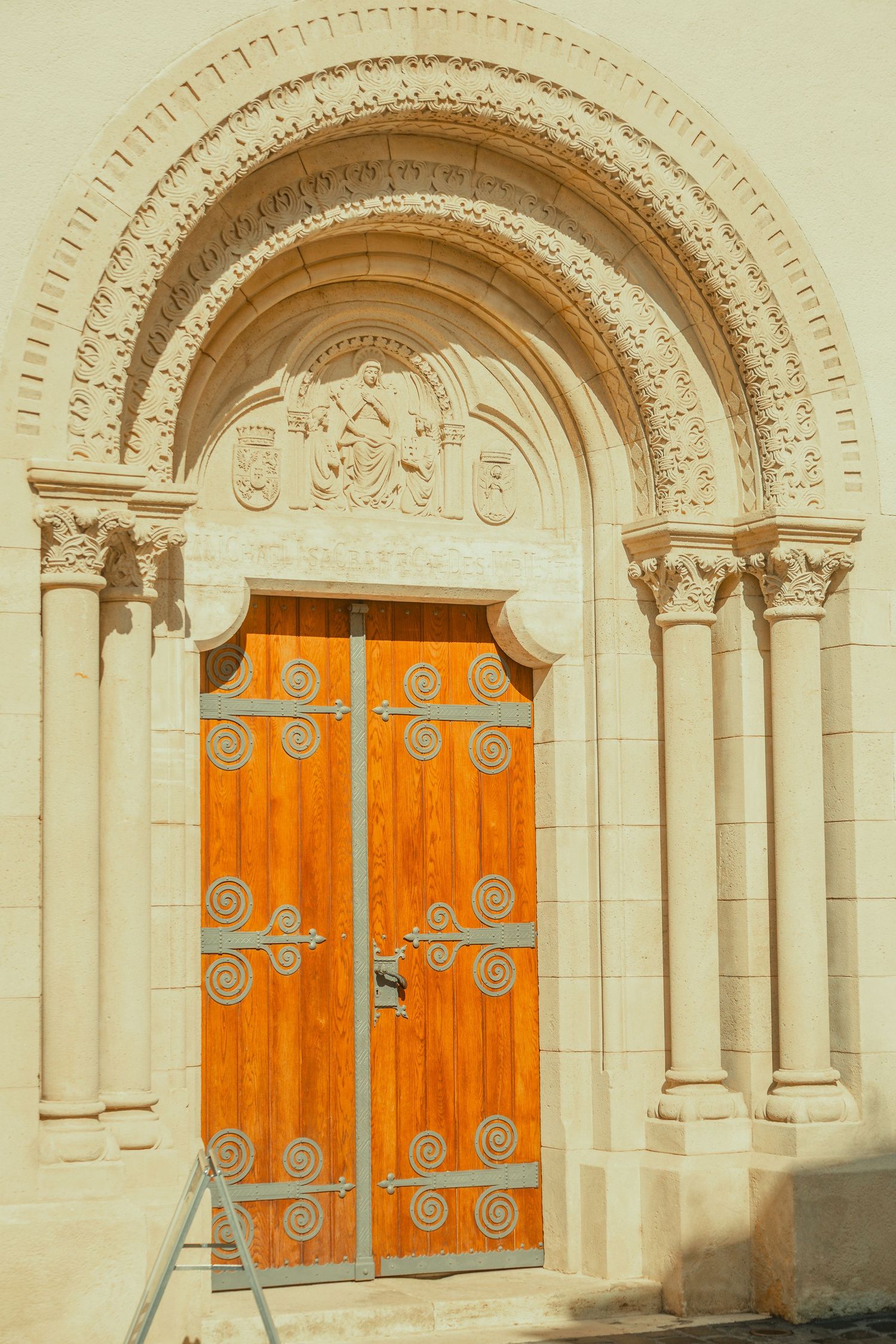 Ornate Romanesque stone archway with wooden doors featuring decorative iron spiral hinges at a historic church.