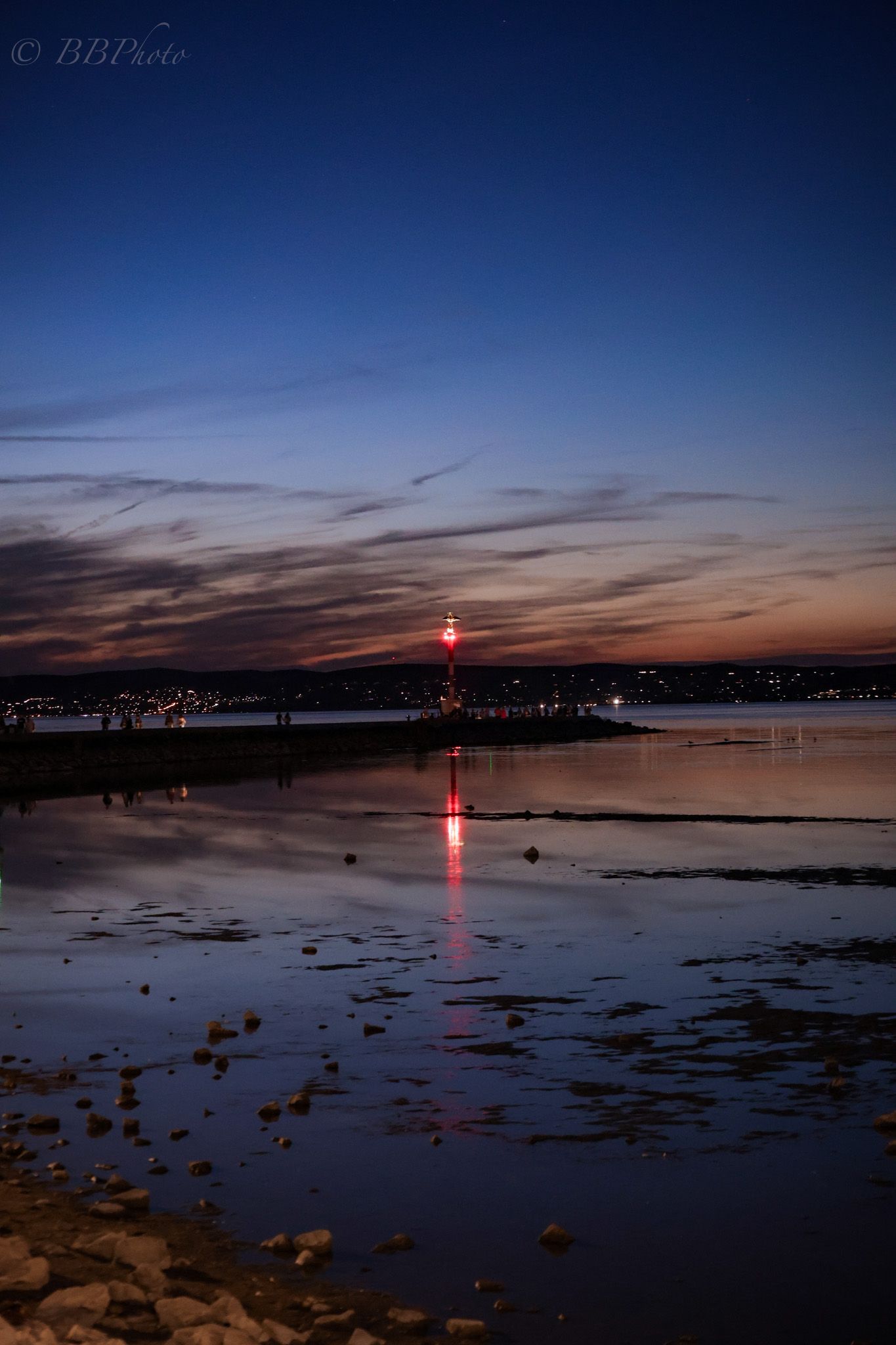 Stunning twilight reflection of a red lighthouse on calm water with dramatic blue and orange sunset sky.