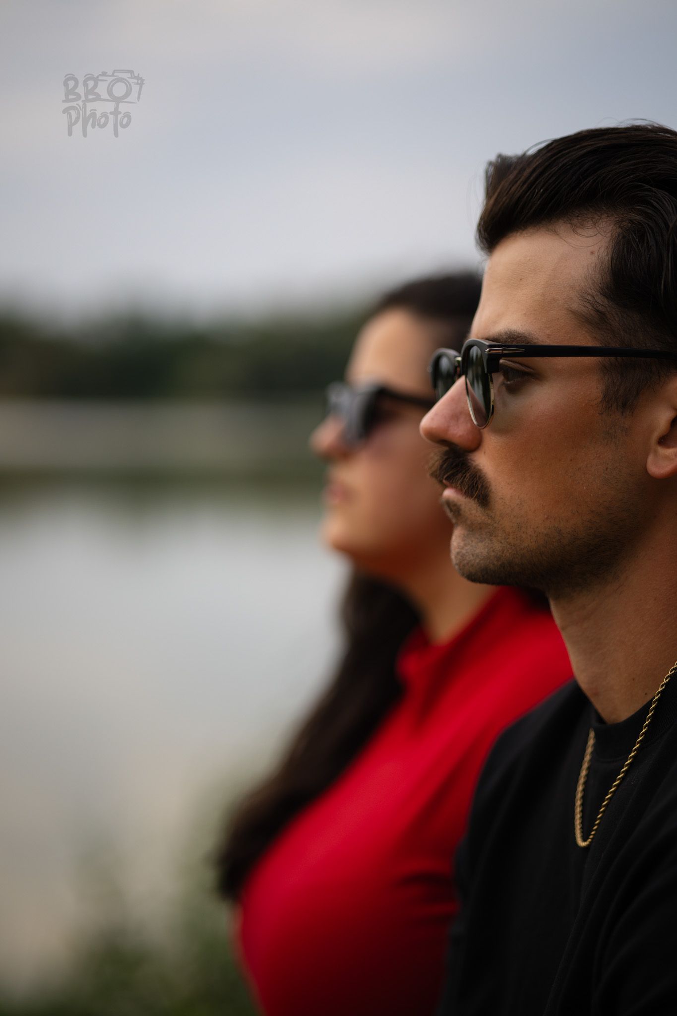 Side profile of a man and woman both wearing sunglasses near a lake.