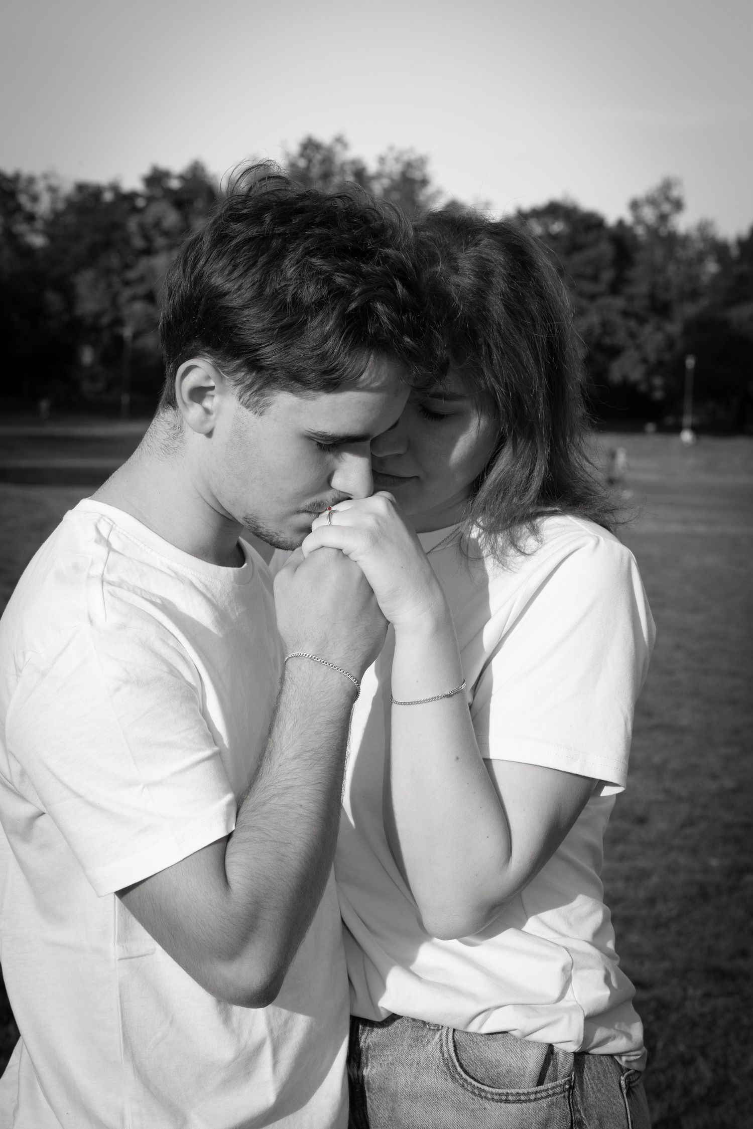 Black and white photo of a young couple sharing a tender moment outdoors in a park setting.