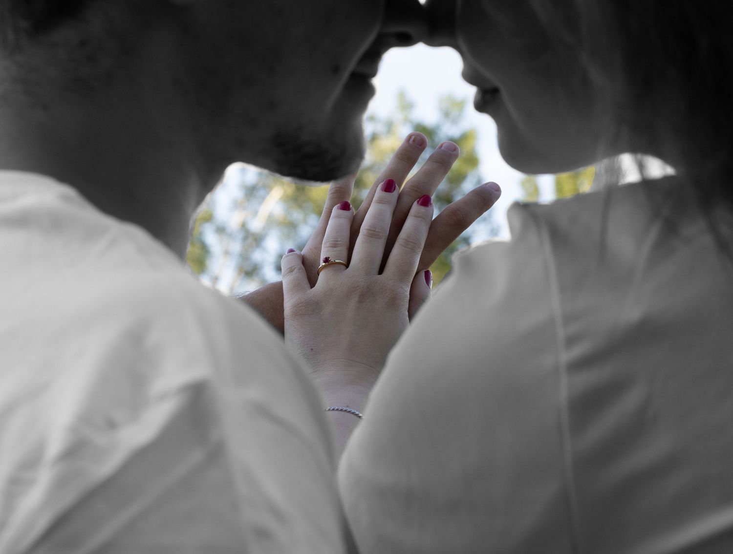 Couple sharing an intimate moment, hands intertwined showing engagement ring, black and white romantic wedding photo.