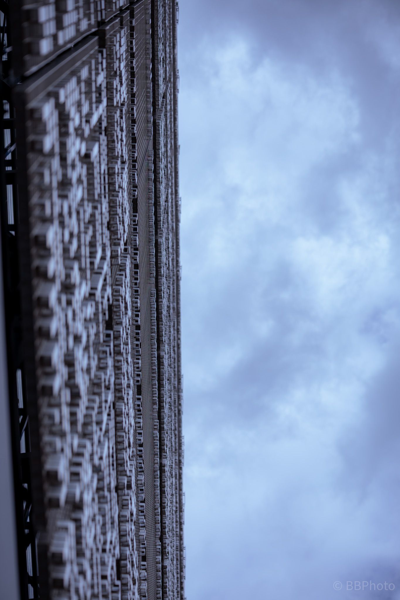 Looking up at a tall building corner with repetitive architectural details against a moody cloudy blue sky.