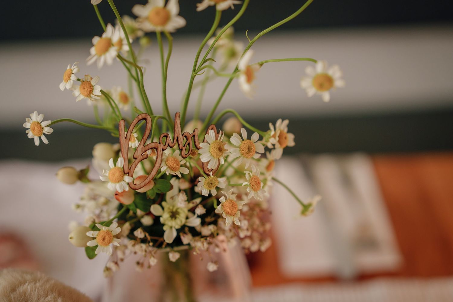 Close-up of a small vase with delicate white daisy wildflowers and a decorative cursive wooden sign centerpiece.