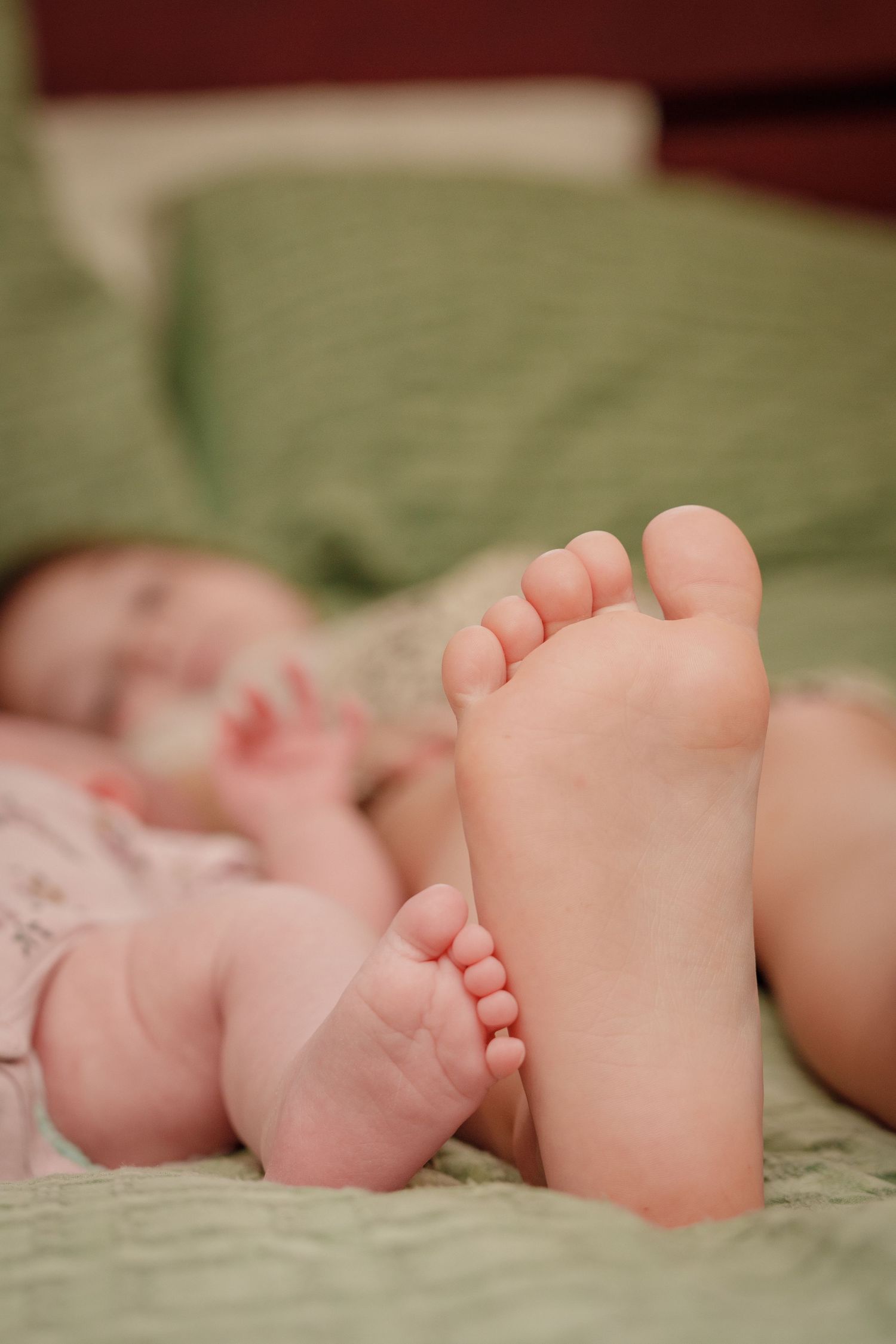 Close-up of a newborn baby's tiny feet in focus, with the infant lying on a green bed in the background.