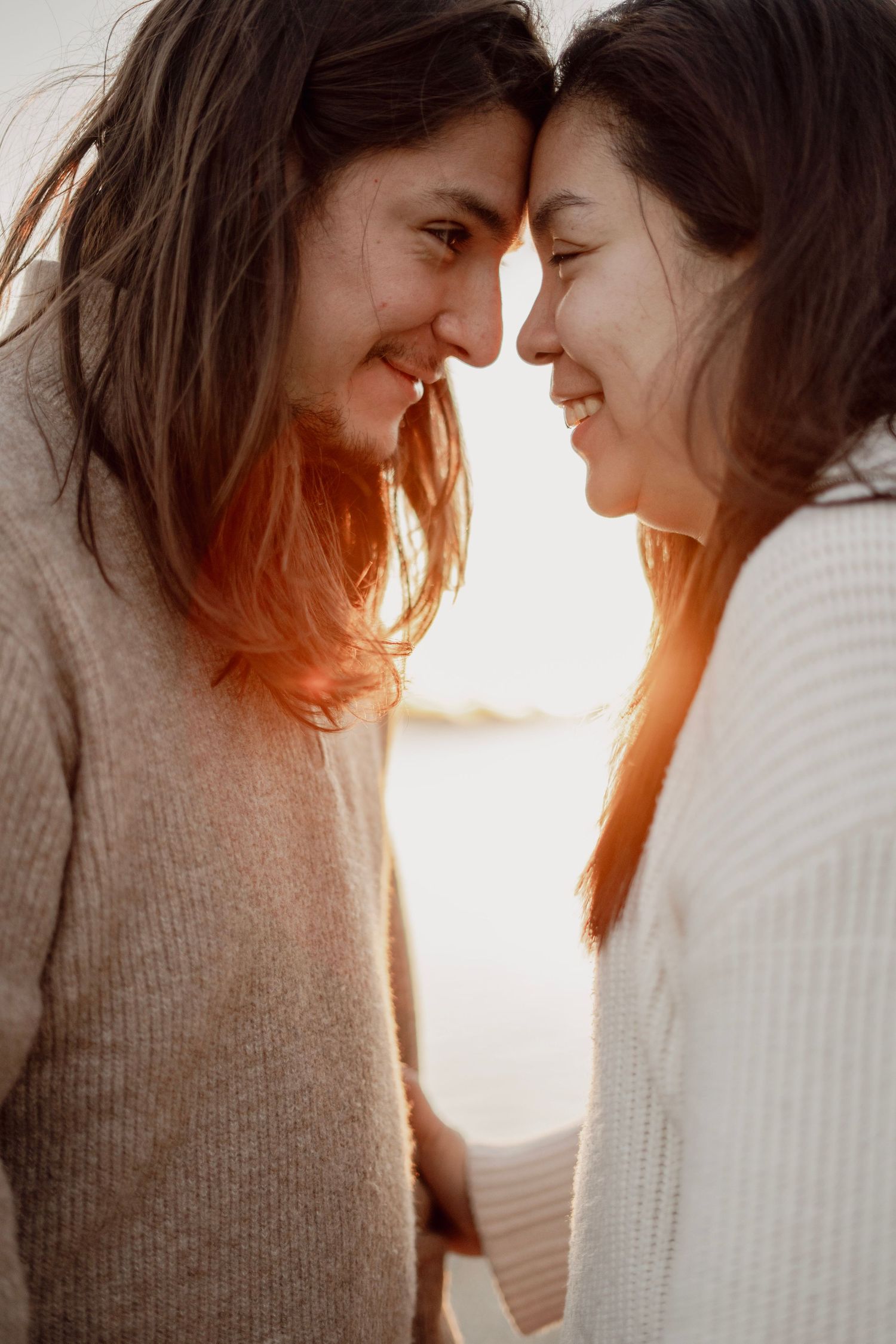 Two smiling women touch foreheads tenderly in a warm golden sunset portrait.