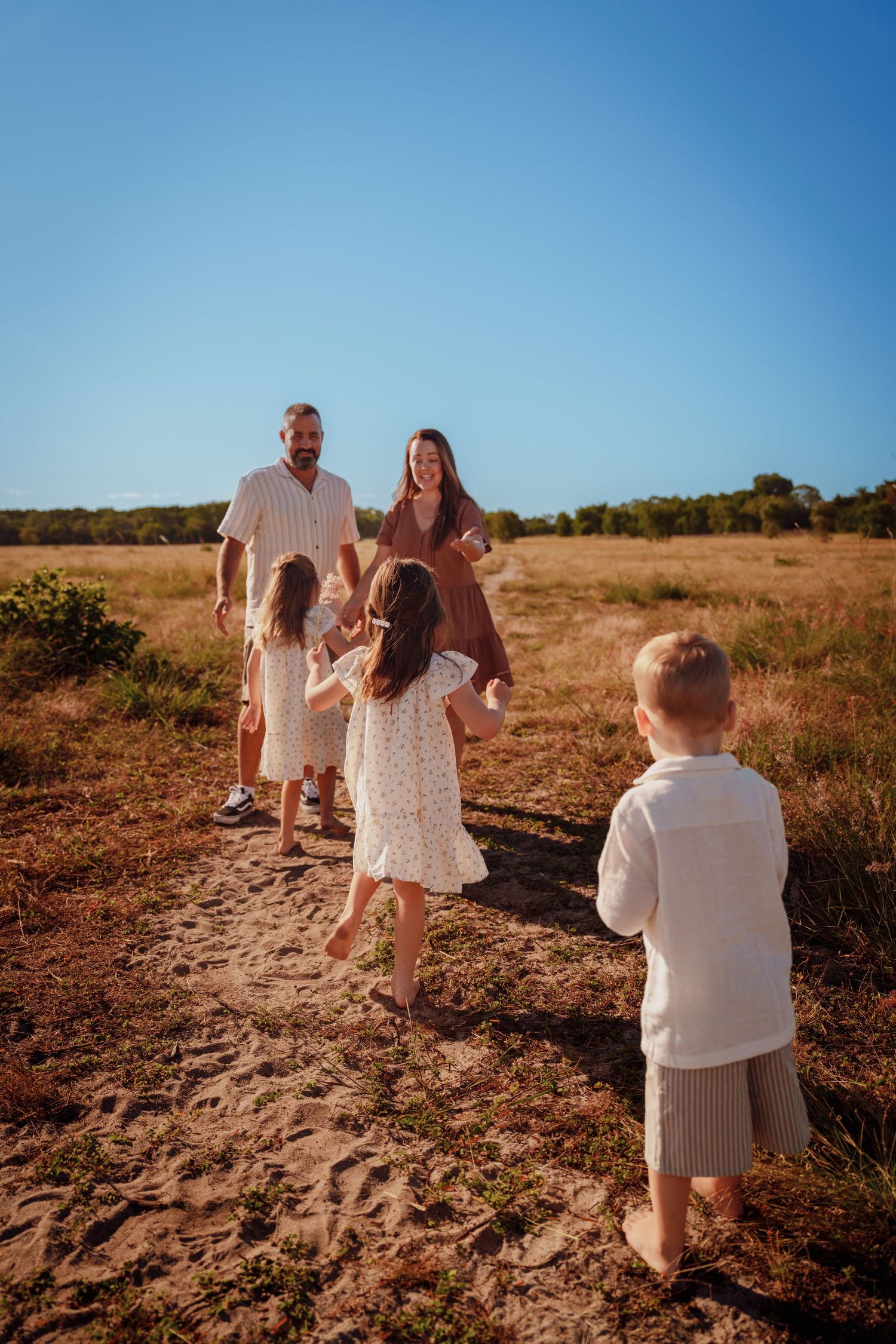 Happy family with three children playing on a sandy path in a golden field under a clear blue sky.