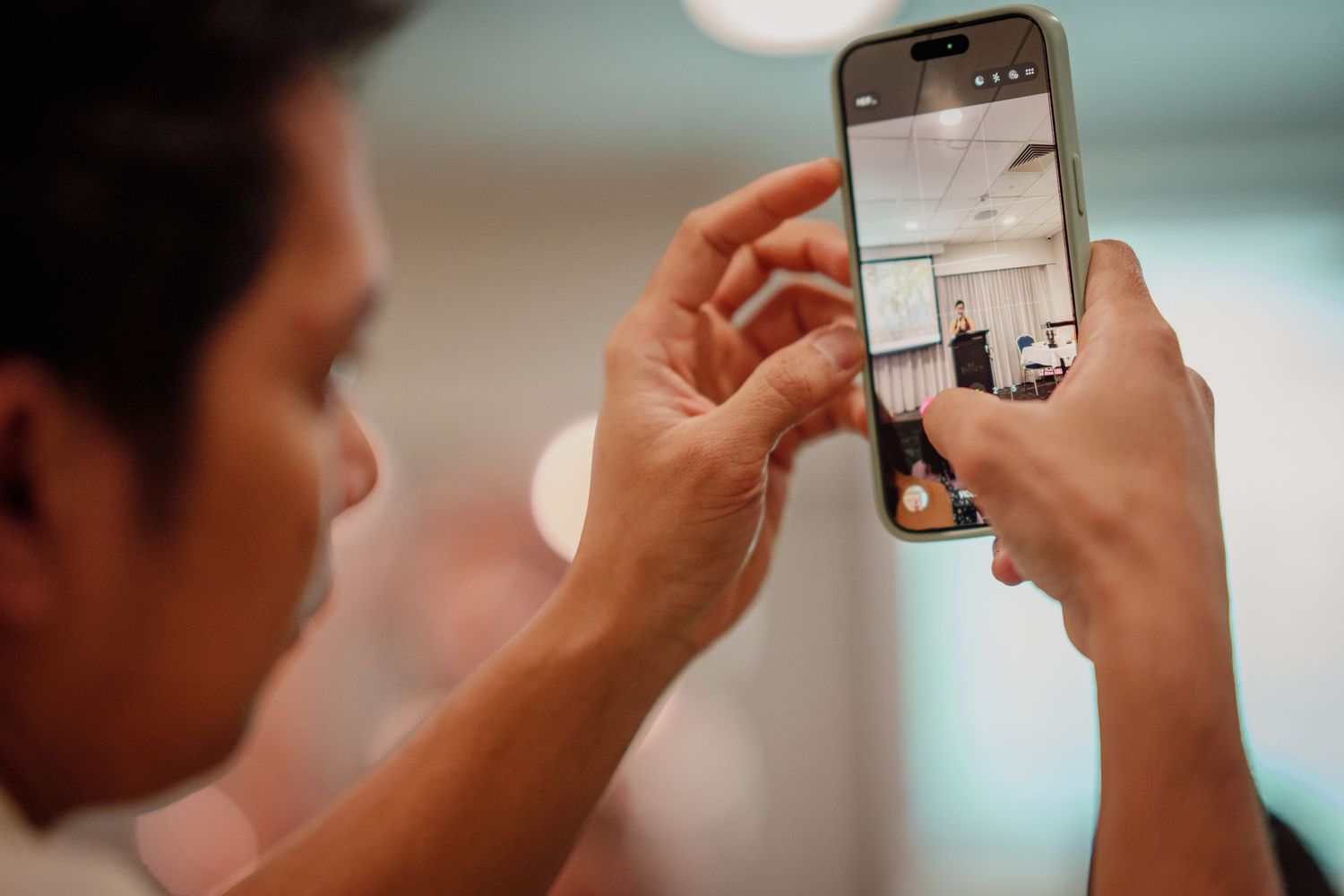 A man holds a smartphone horizontally, photographing a room interior with the camera app open on the screen.