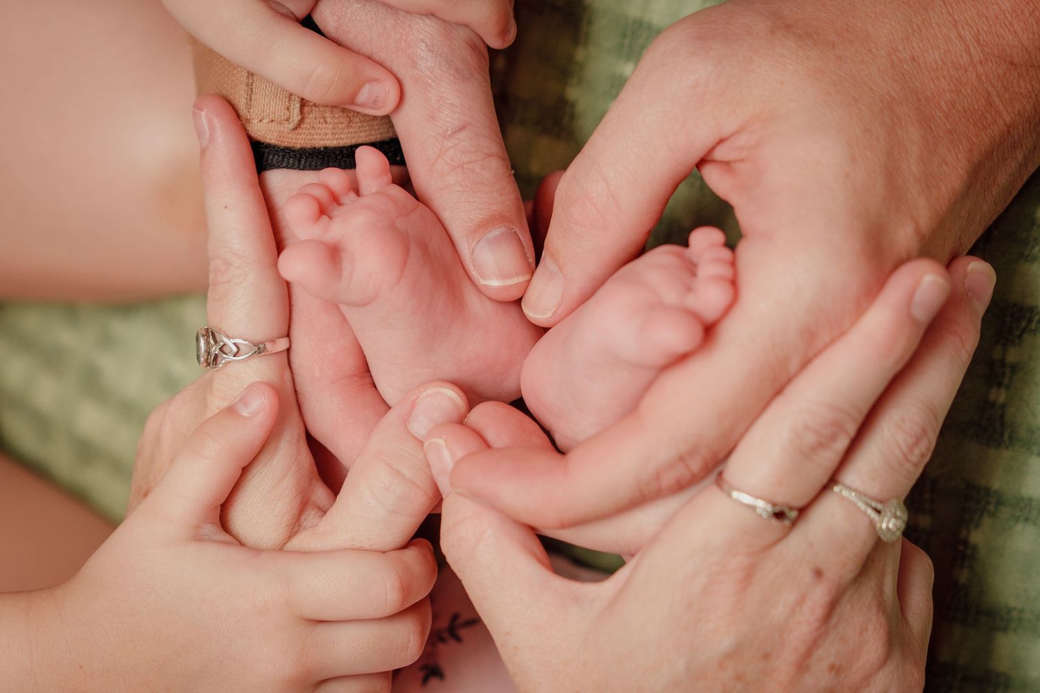 Two parents and a child gently cradle a newborn baby's tiny feet in their hands, showcasing a heartwarming family moment.