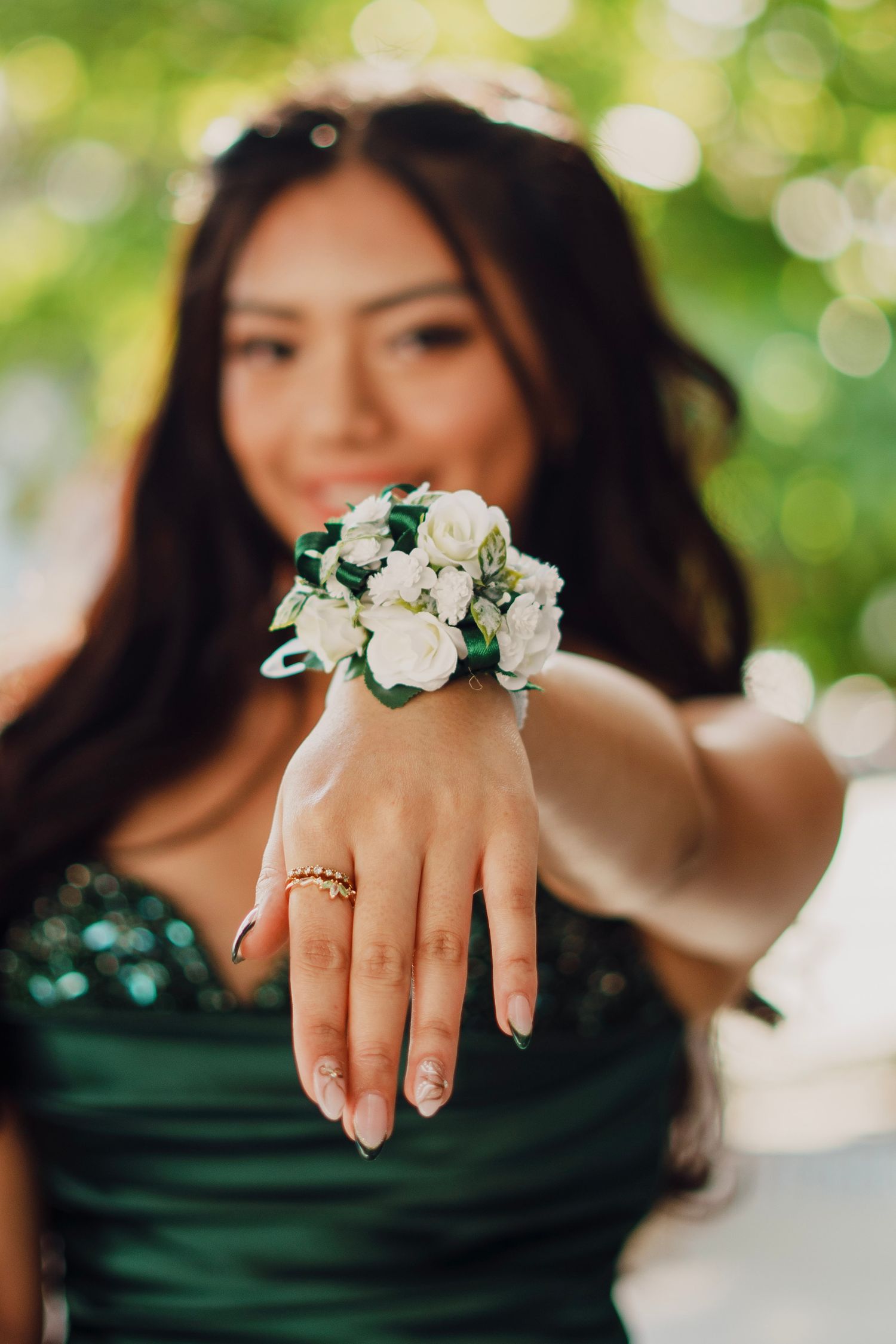 Young woman in green dress showing wrist corsage with white roses at prom.
