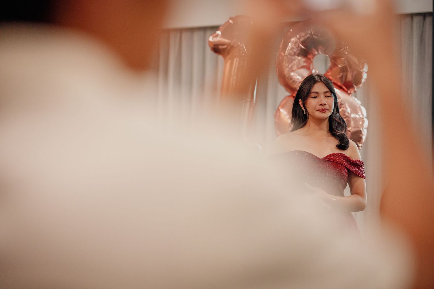 Young woman in elegant off-shoulder dress with floral headpiece reflected in mirror during bridal preparation.