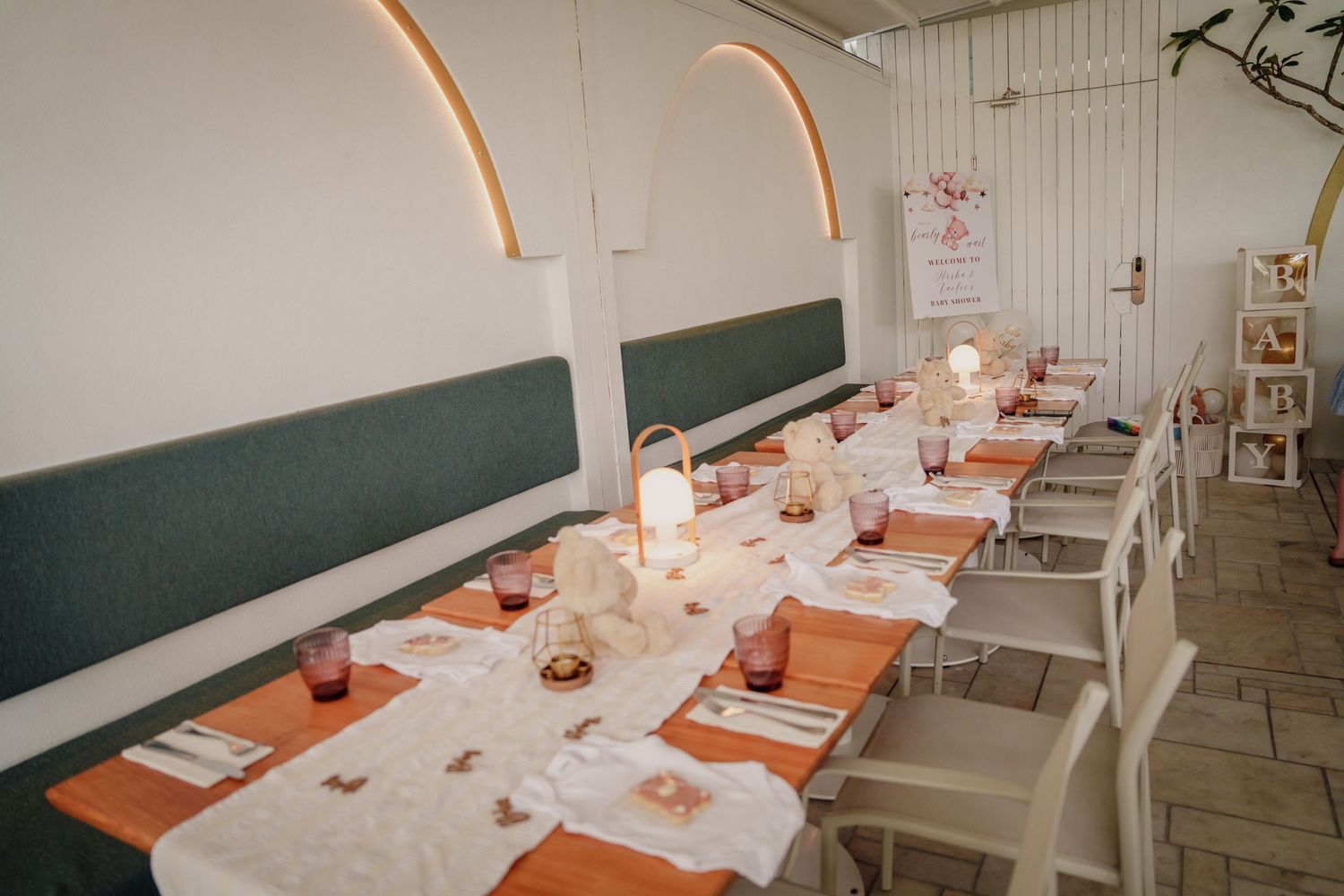 Elegant restaurant dining room with long tables set for an event, featuring orange runners, candles, and arched wall details.