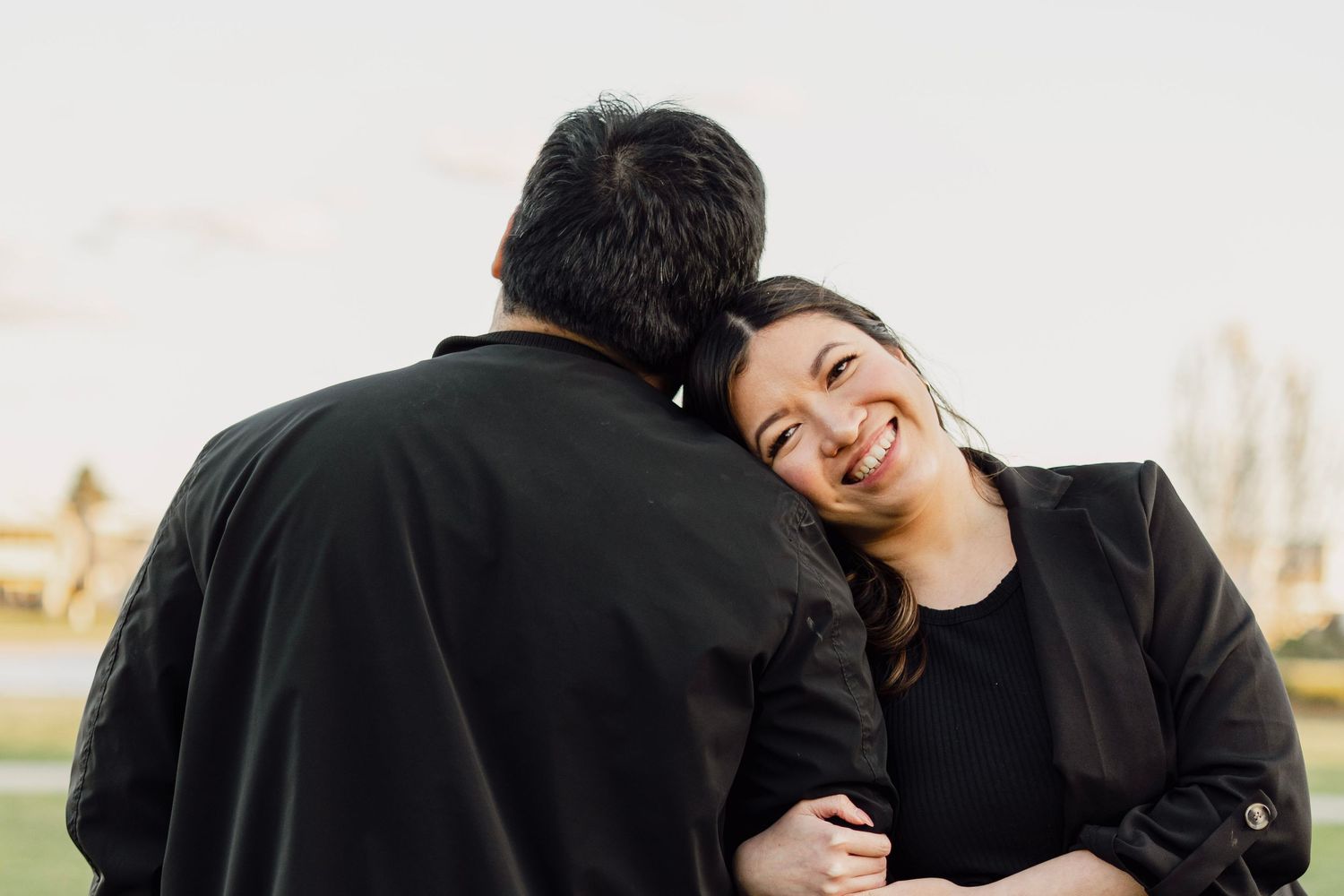 A smiling woman leans her head on a man's shoulder during a romantic outdoor couples photo session.