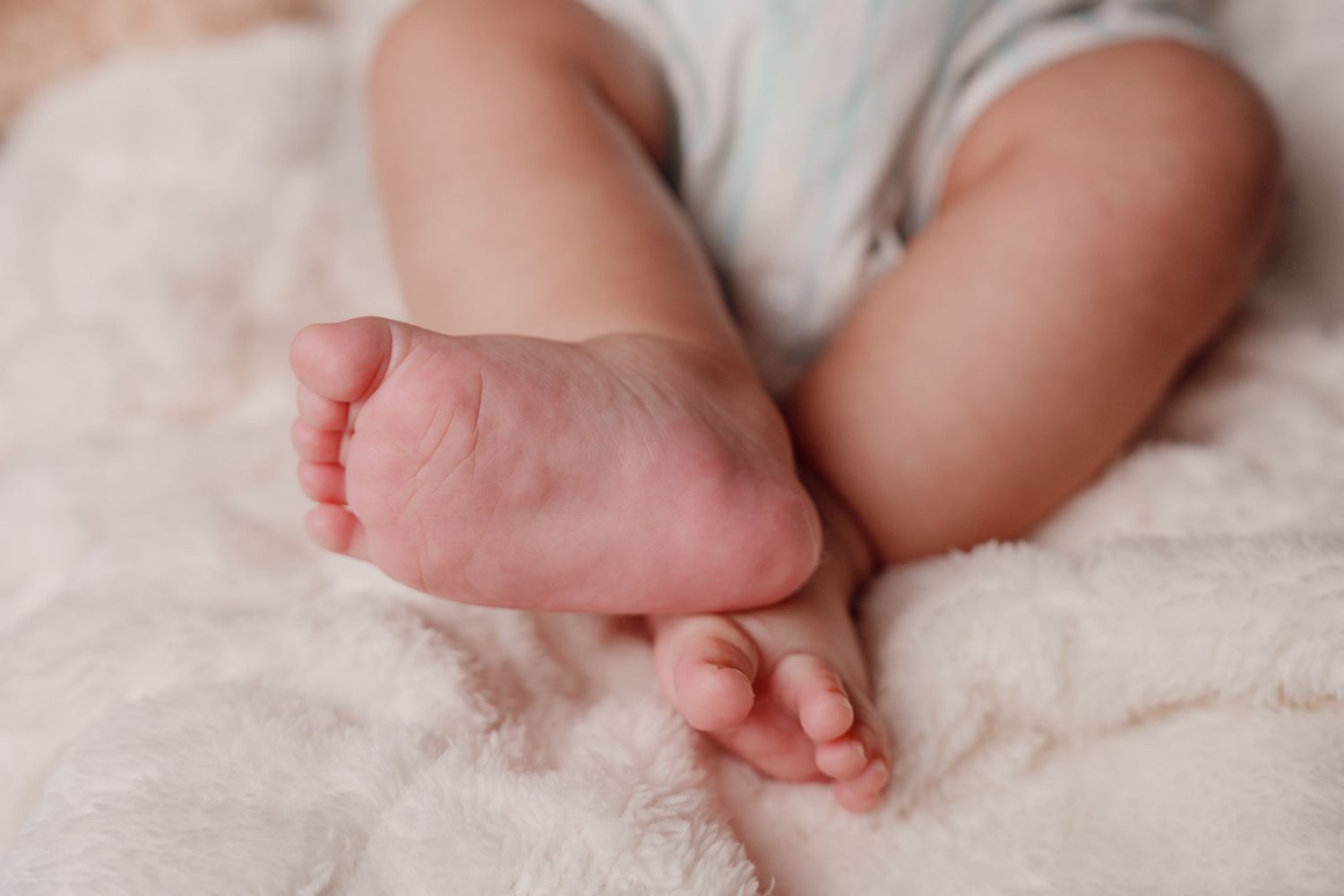 Close-up of tiny newborn baby feet resting on a soft pink fluffy blanket.