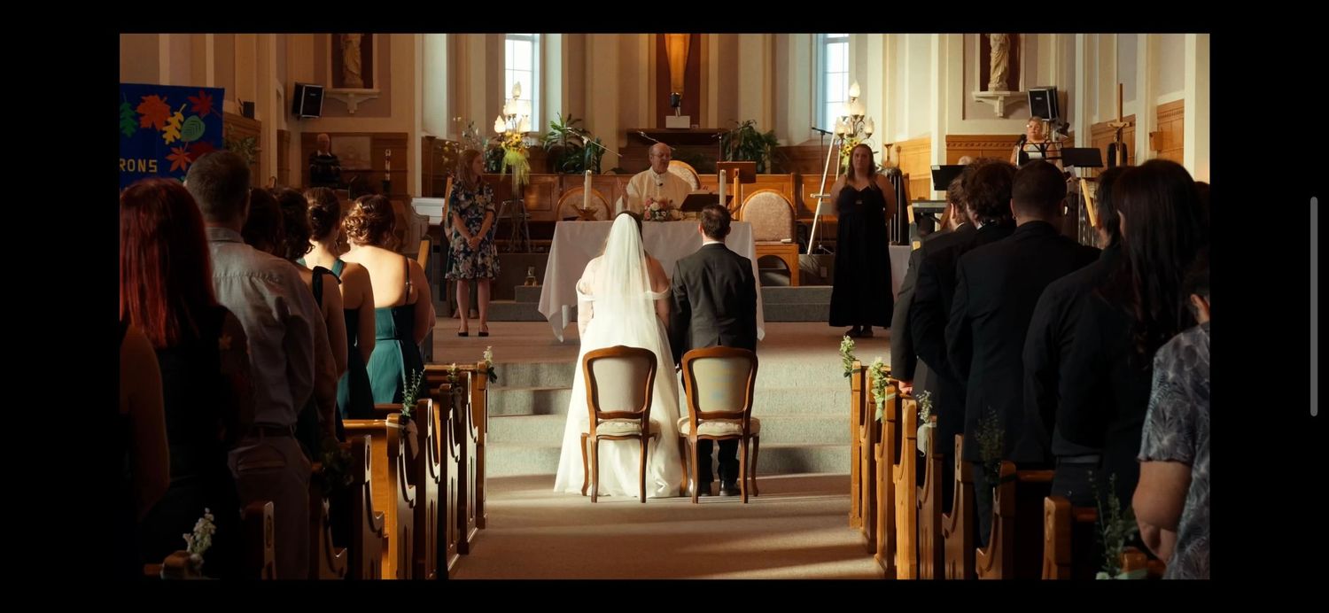 Wedding ceremony inside a church with bride and groom seated at altar surrounded by guests in pews.