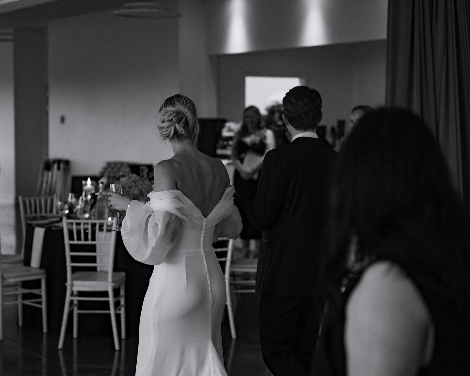Bride and groom walking into wedding reception venue in elegant black and white photography.