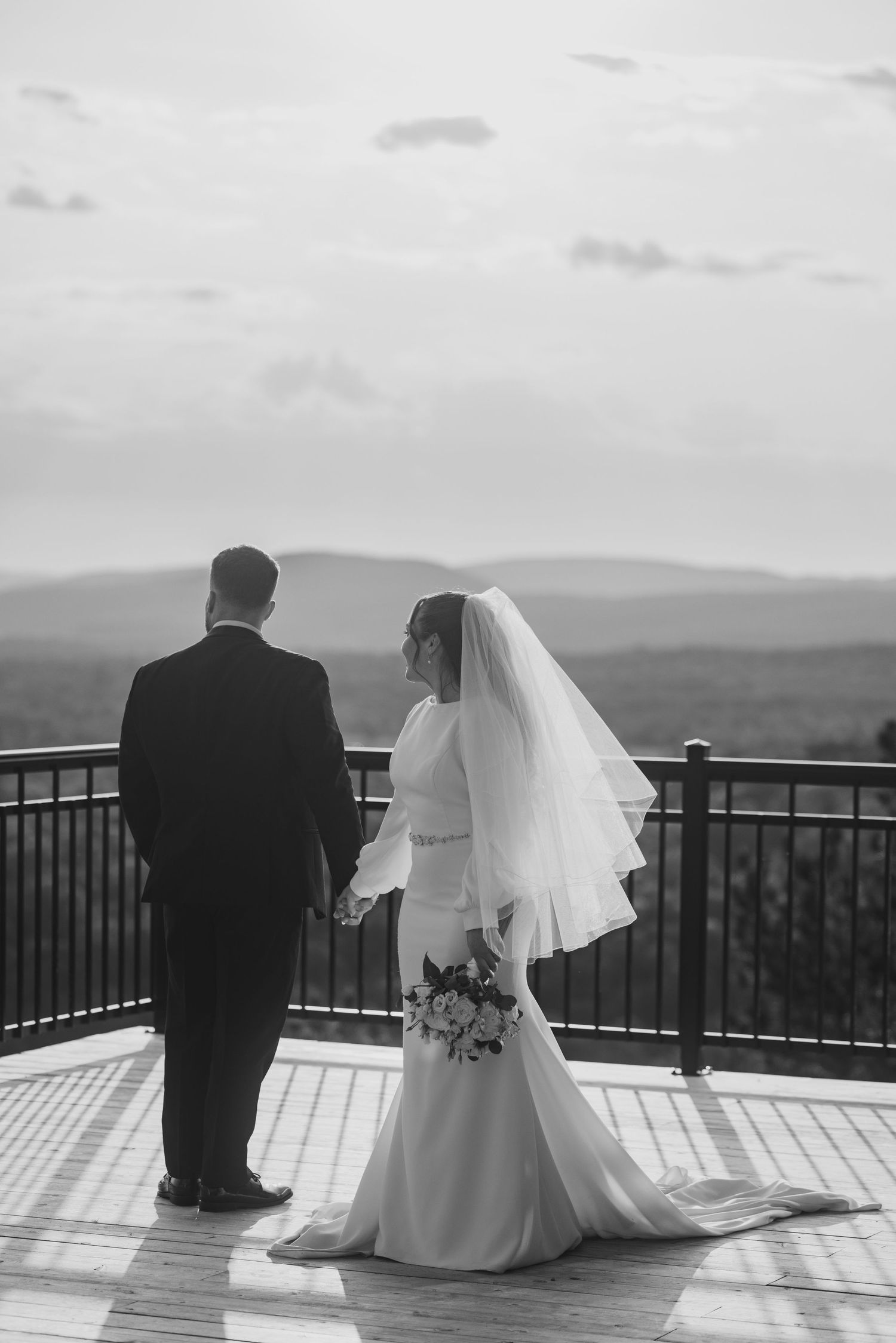 Black and white bride and groom holding hands on scenic overlook deck.