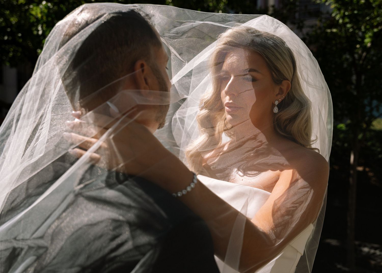 Bride and groom share an intimate moment under a flowing wedding veil outdoors.