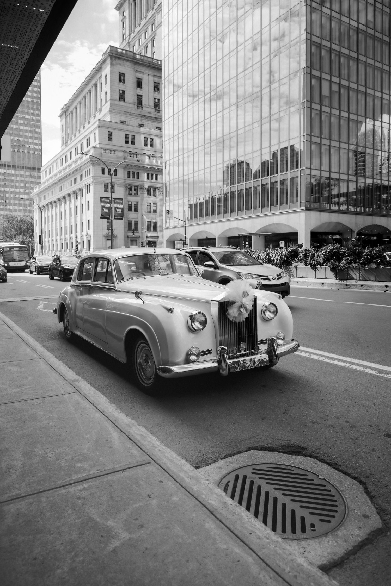 Vintage white Rolls-Royce wedding car decorated with flowers driving through urban city street.
