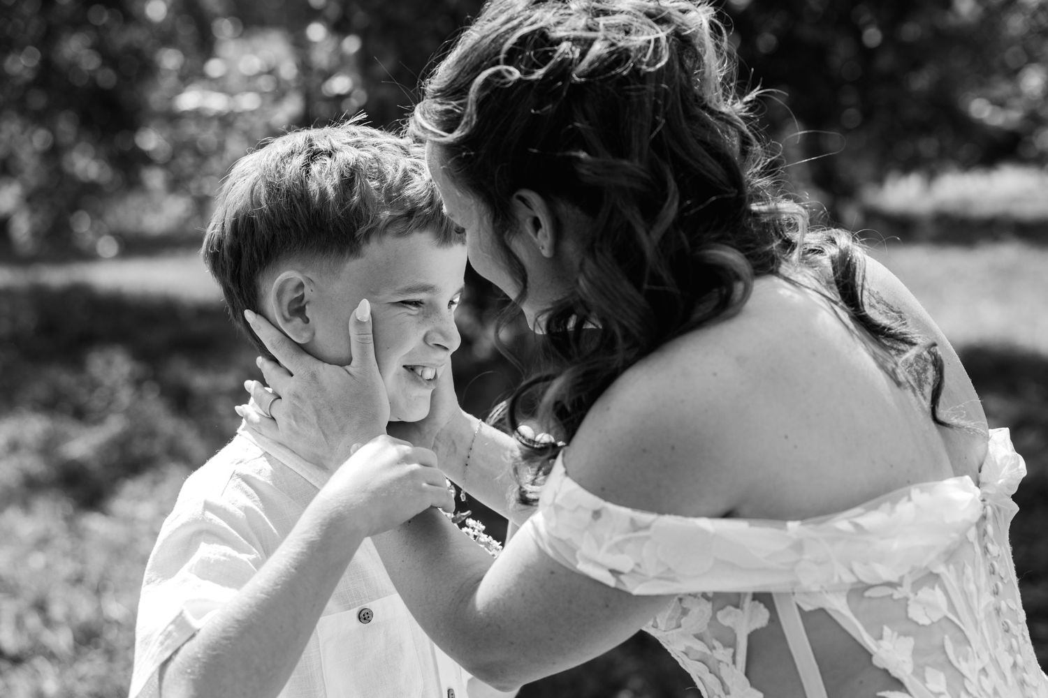 Black and white photo of a mother tenderly holding her young son's face as they share a joyful moment outdoors.