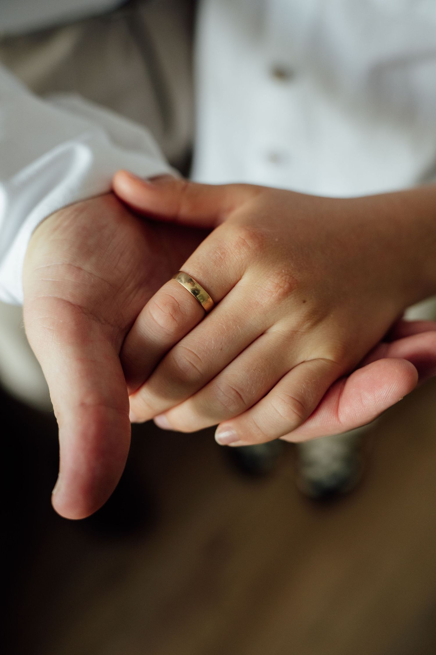 Close-up of newlyweds holding hands with a gold wedding band on the bride's finger.