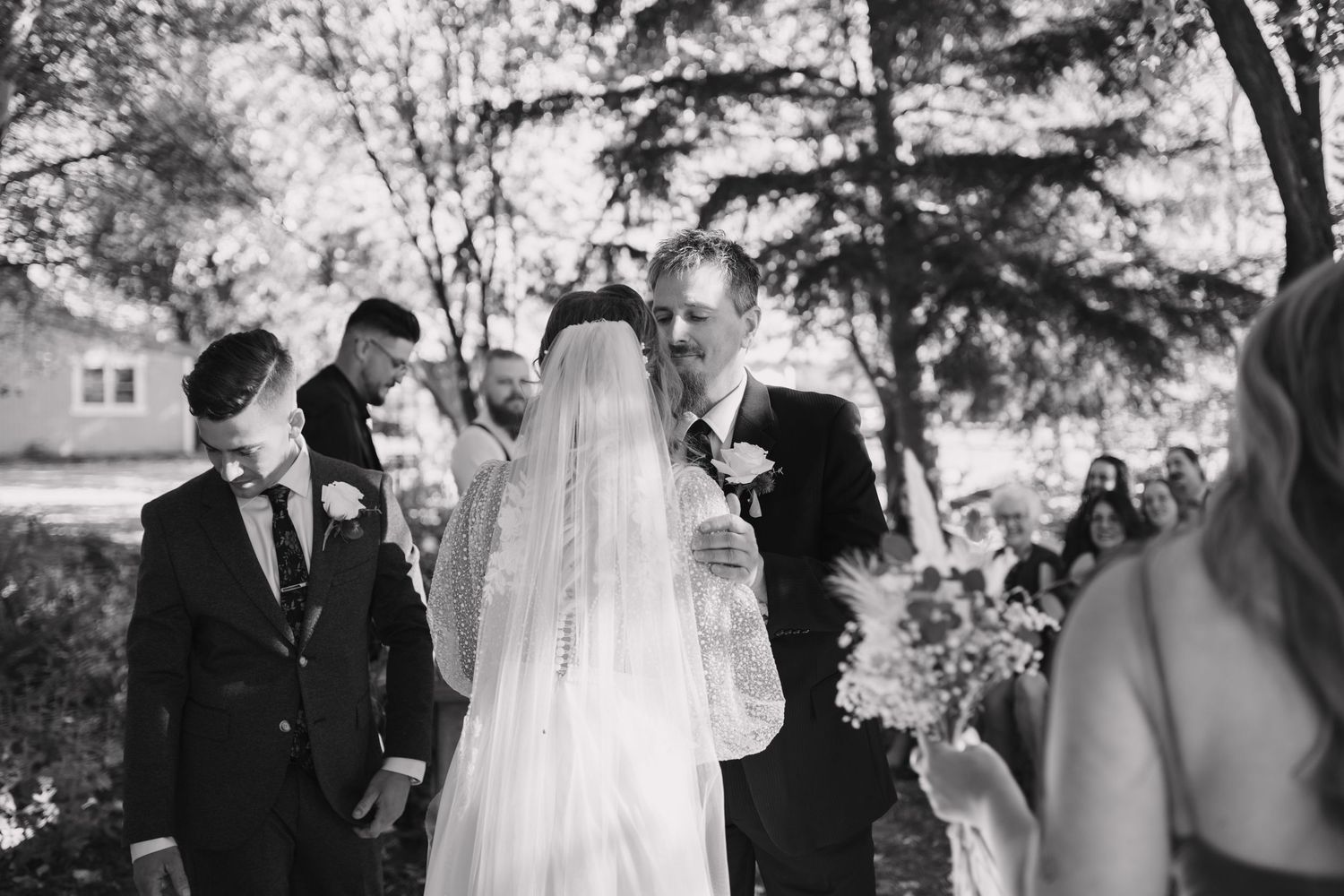 Bride and groom share a tender moment during an outdoor wedding ceremony surrounded by guests.