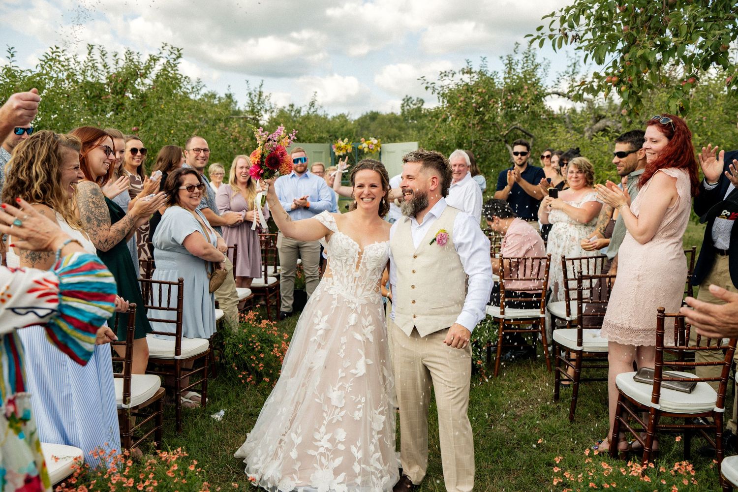 Newlyweds walk joyfully down the aisle as guests celebrate at a lush outdoor garden wedding ceremony.