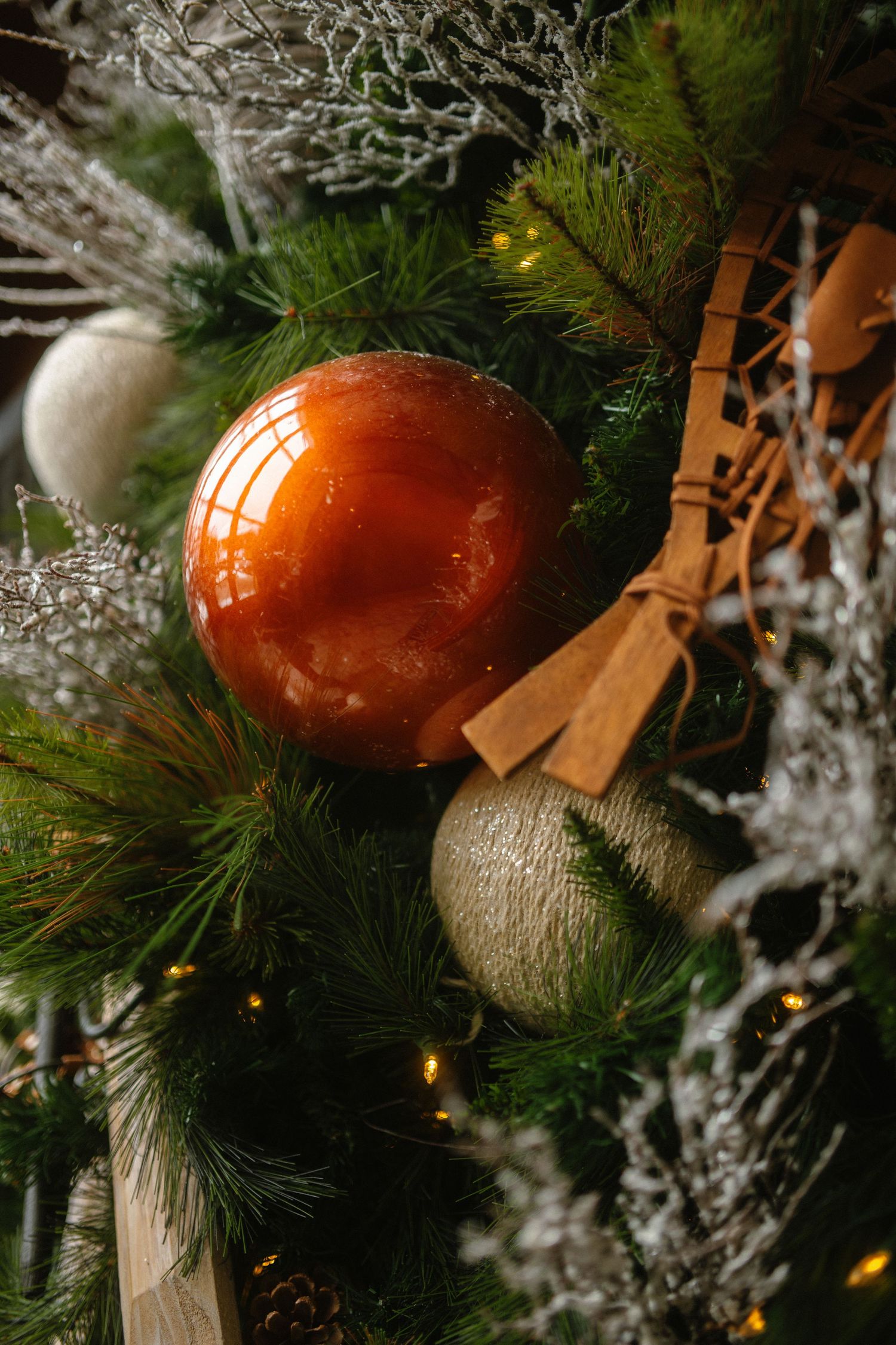 Close-up of Christmas tree with glossy amber ornament, silver balls, and wooden snowshoe decoration.