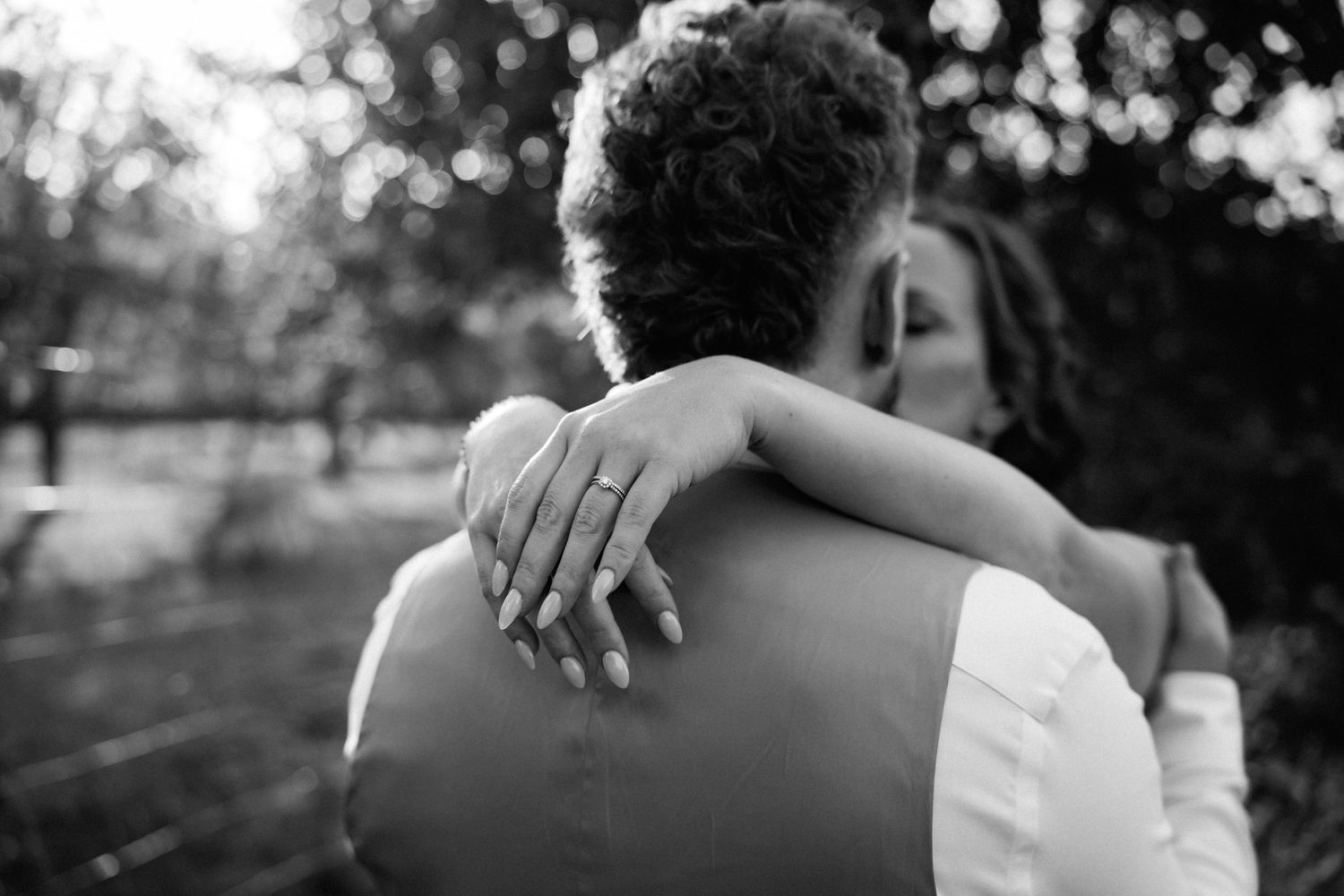 Black and white photo of bride embracing groom showing wedding ring on her finger.